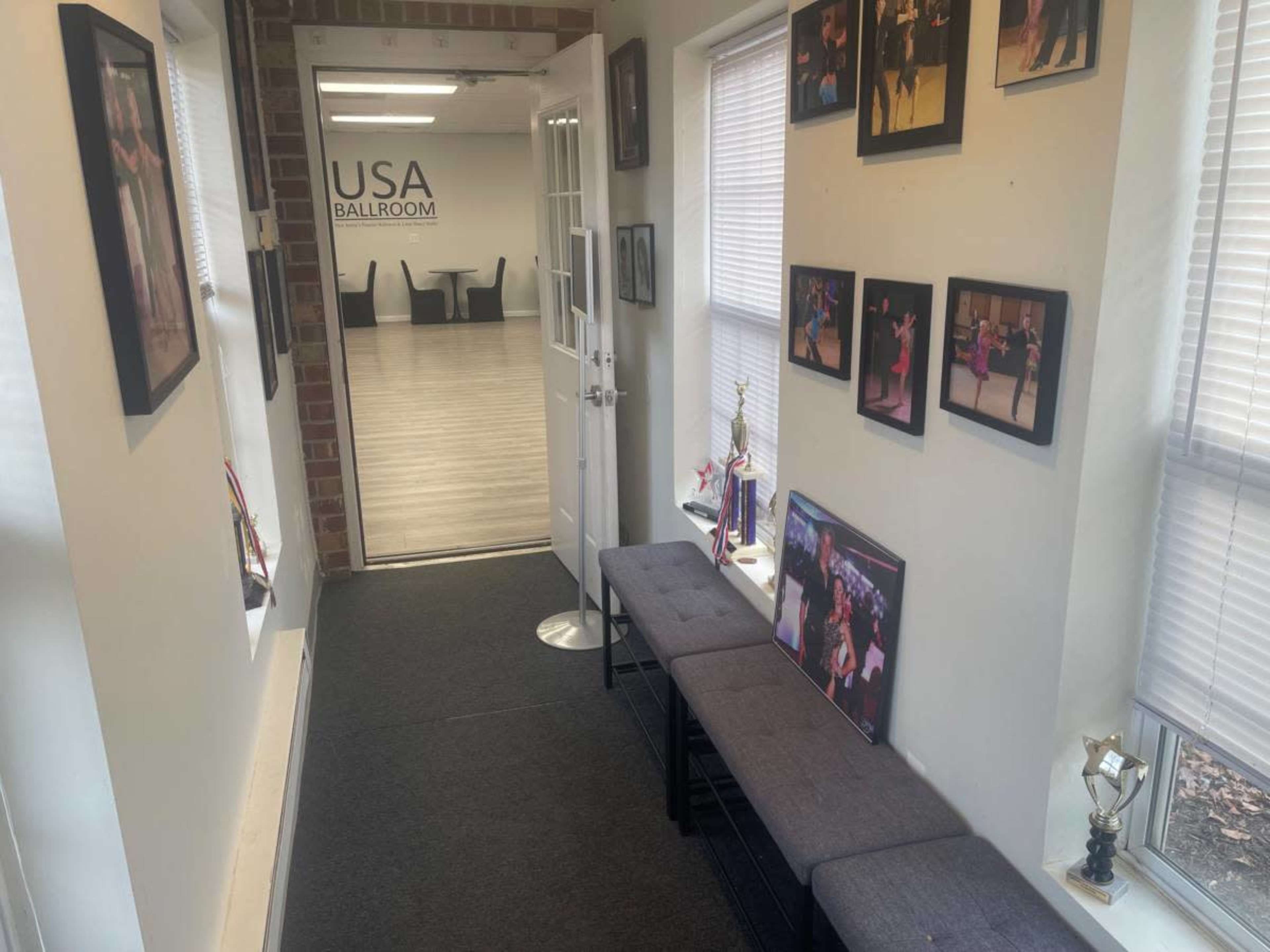 A narrow hallway leads to an open ballroom, lined with framed photos and trophies along the walls.