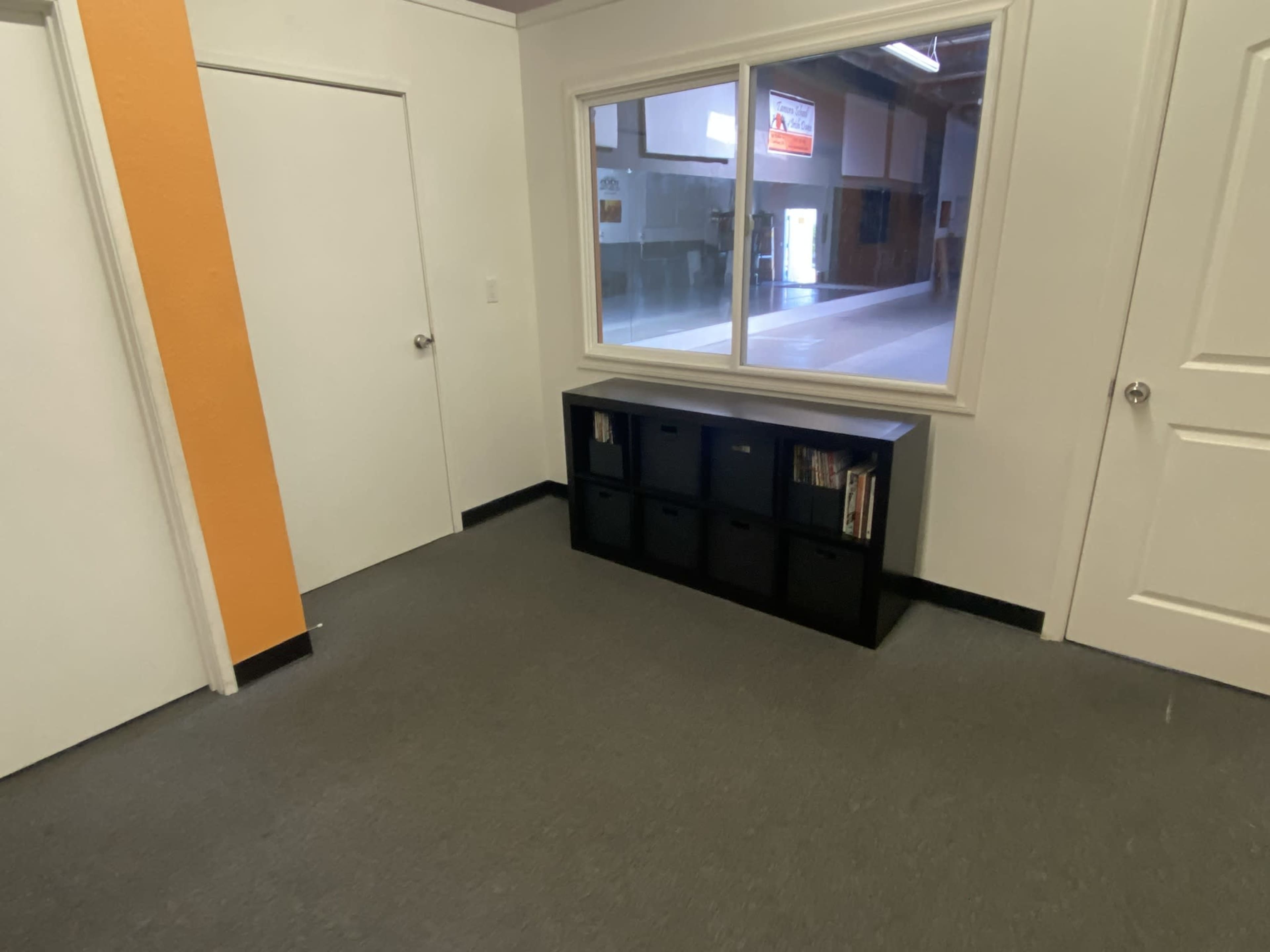 A hallway features a door, a large window, and a black storage unit against the wall.