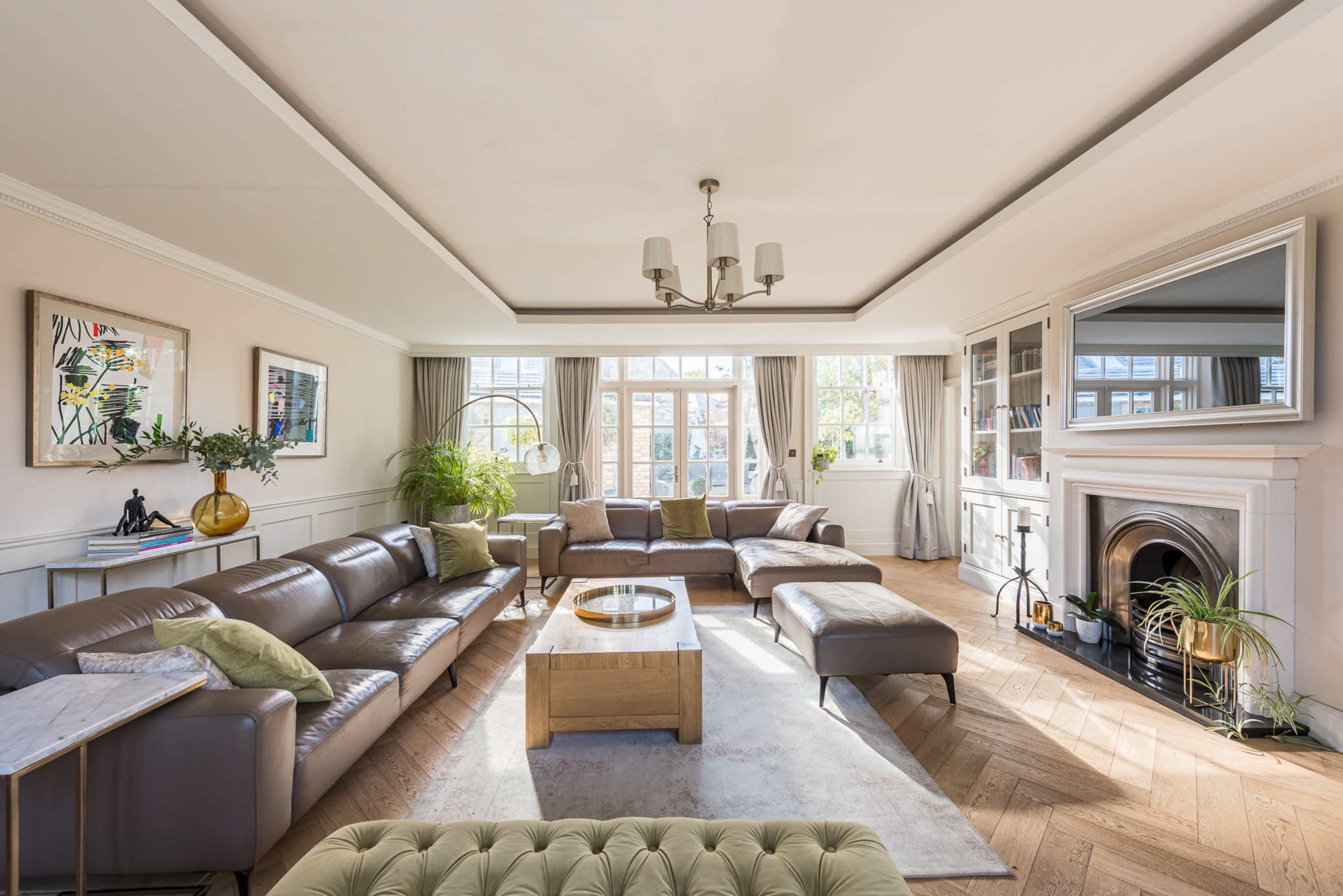 The living room features a spacious layout with a large leather sectional sofa, a wooden coffee table, and a fireplace, all illuminated by natural light from multiple windows.