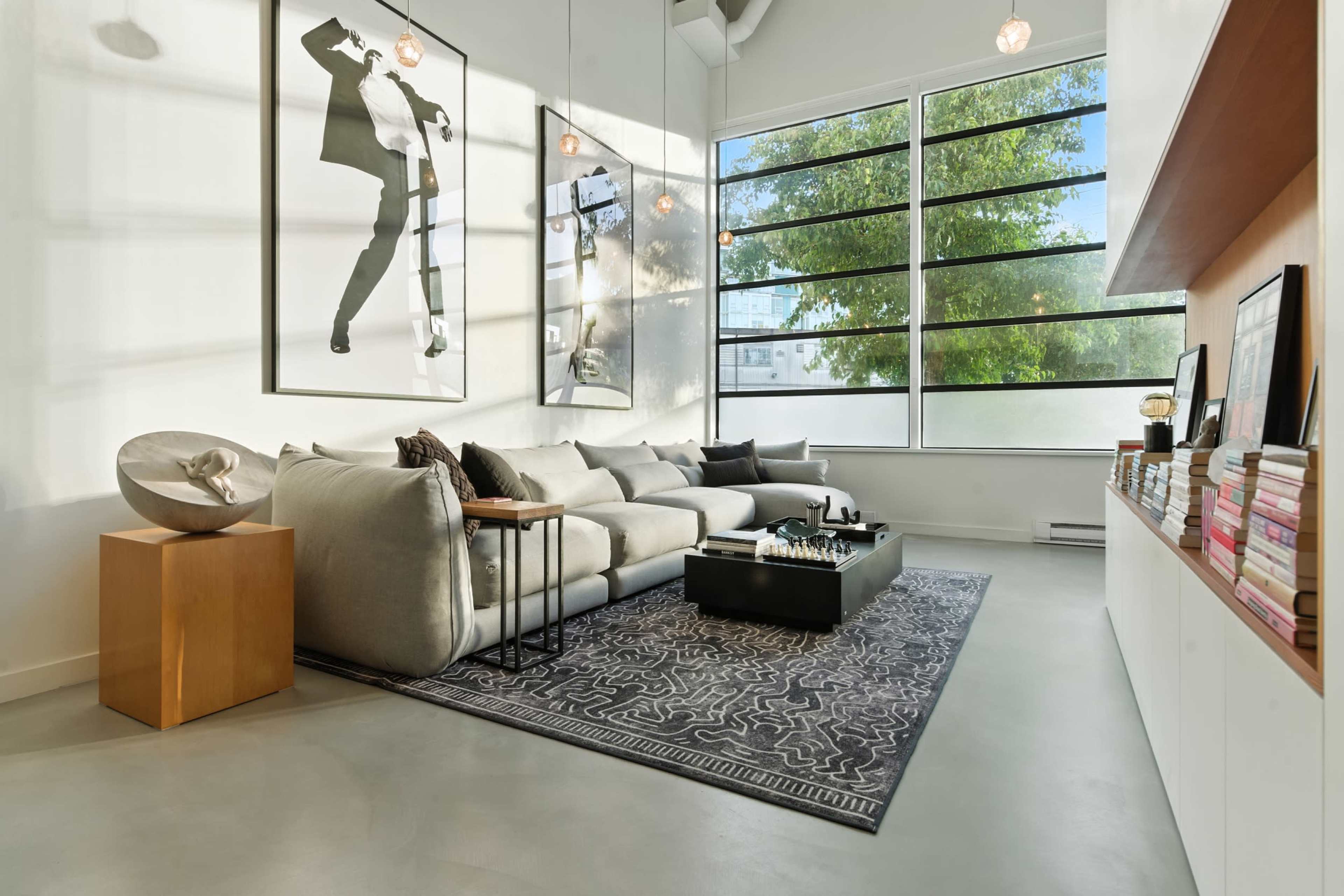 The image shows a modern living room with a gray sectional sofa, a black coffee table, and large windows providing natural light.
