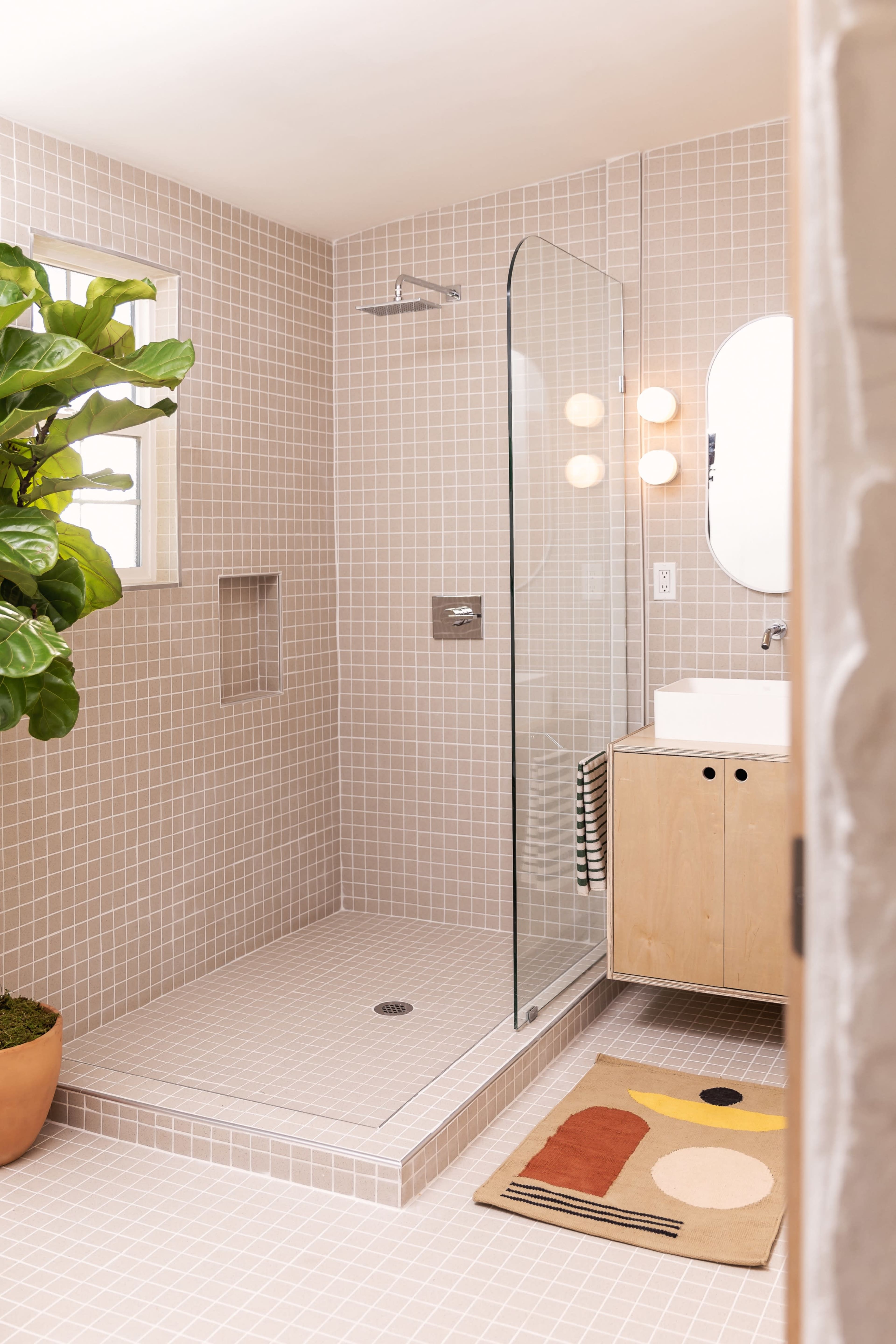 A modern bathroom featuring a glass shower, tiled walls, a wooden vanity, and a potted plant.