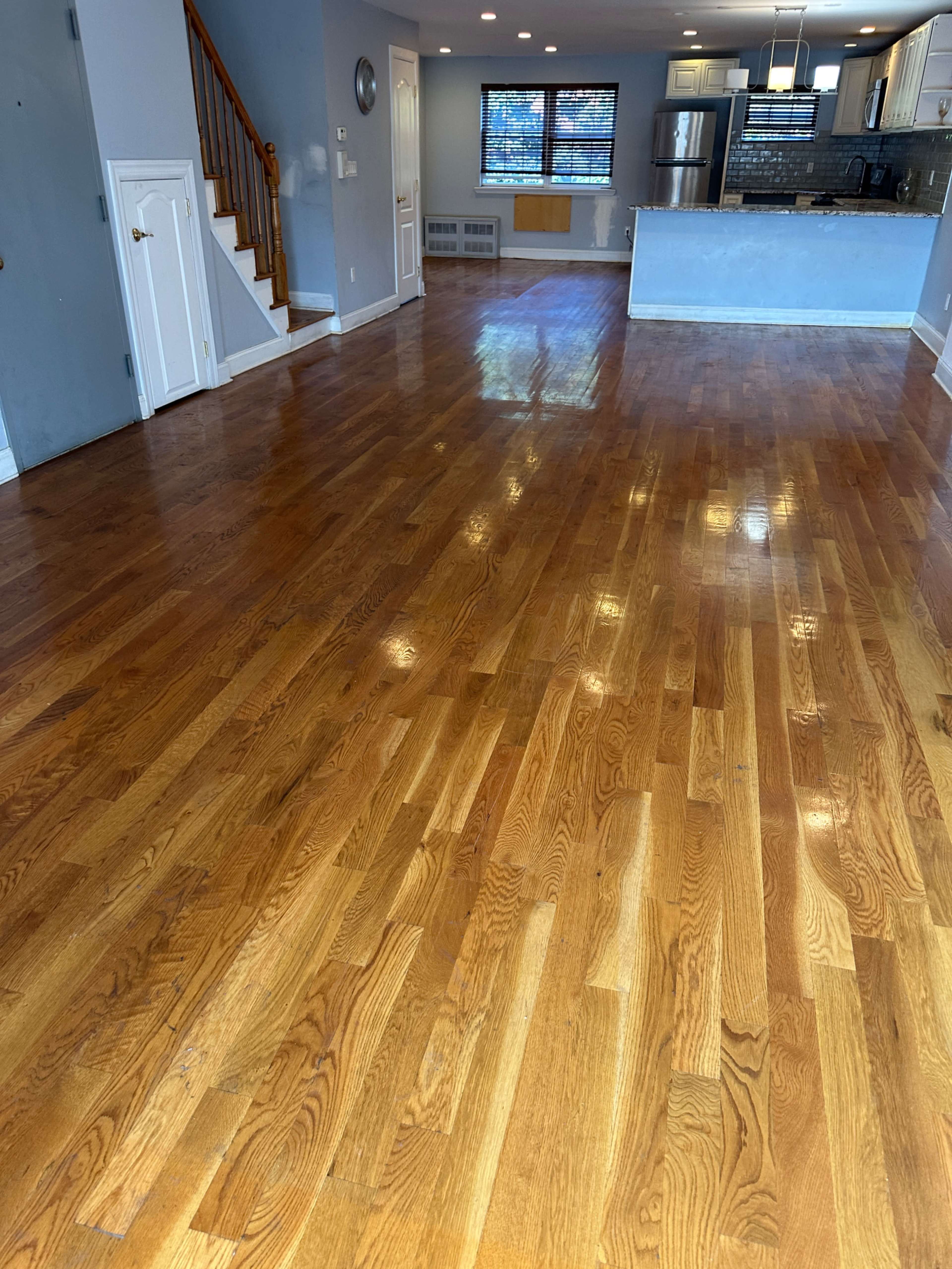 The image shows a hardwood-floored living area with a staircase and kitchen visible in the background.