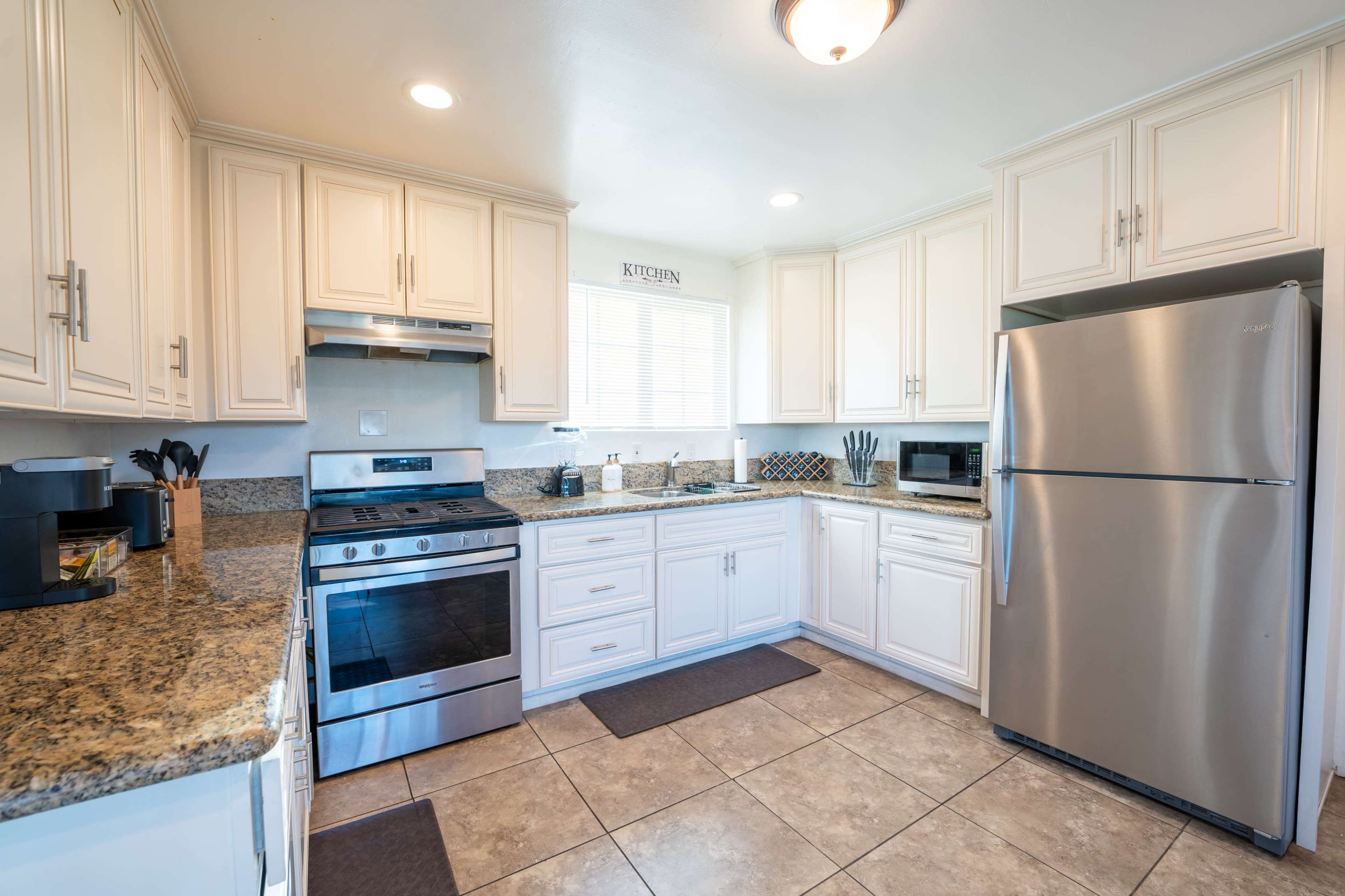 The image shows a modern kitchen with white cabinets, a stainless steel refrigerator, and granite countertops.