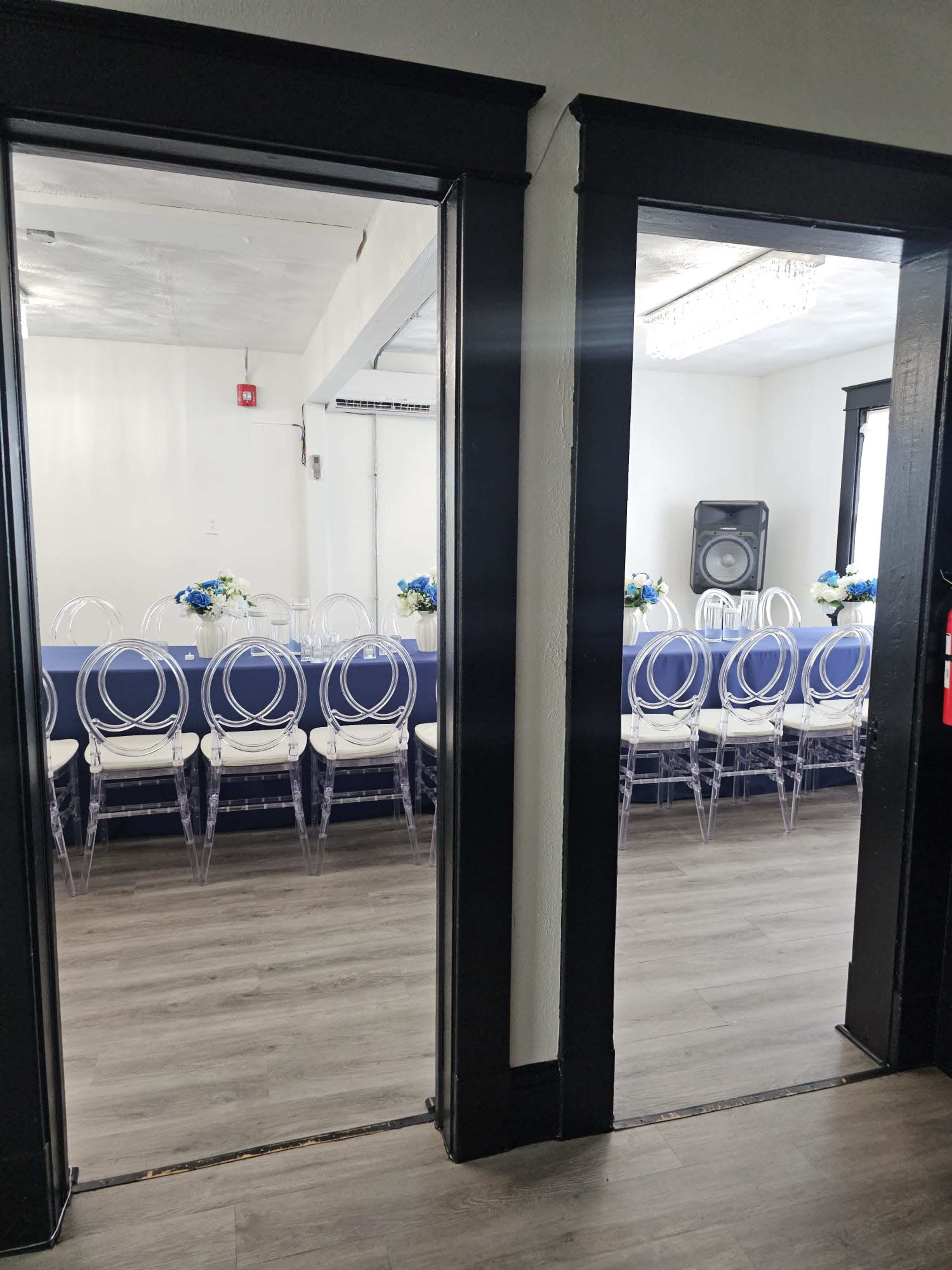 The image shows two doorways leading into a room with clear chairs arranged in rows and decorated with blue flowers on a table.