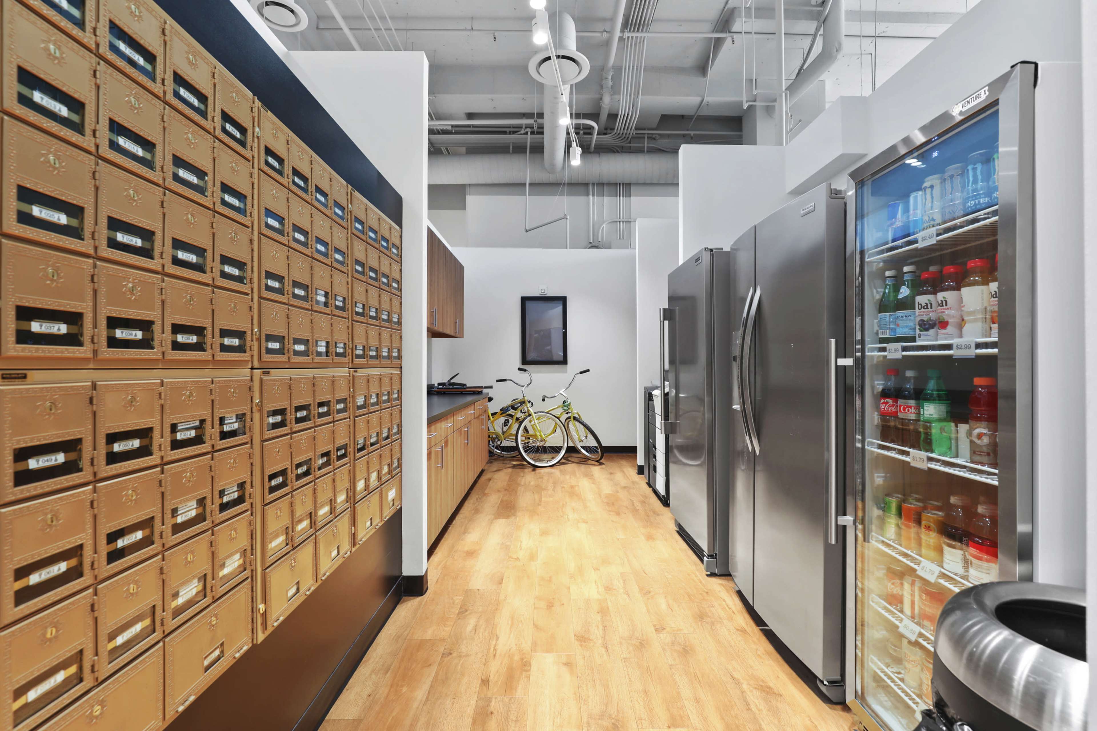 The image shows a hallway with mailboxes on one side and two refrigerators along the opposite wall, with a bicycle parked in the middle.