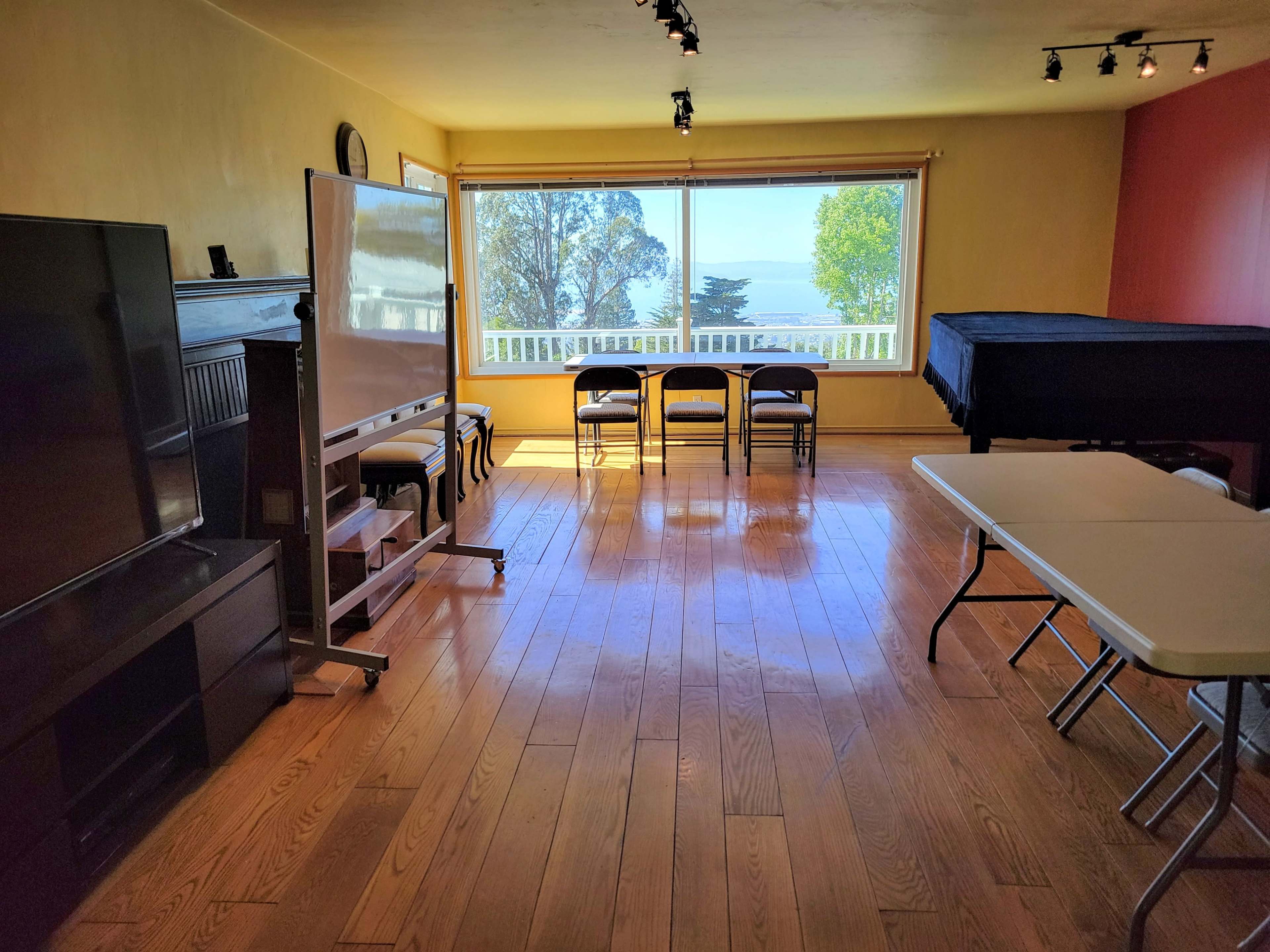 A spacious room features a television, a whiteboard on wheels, chairs arranged for seating, and large windows overlooking a scenic view.
