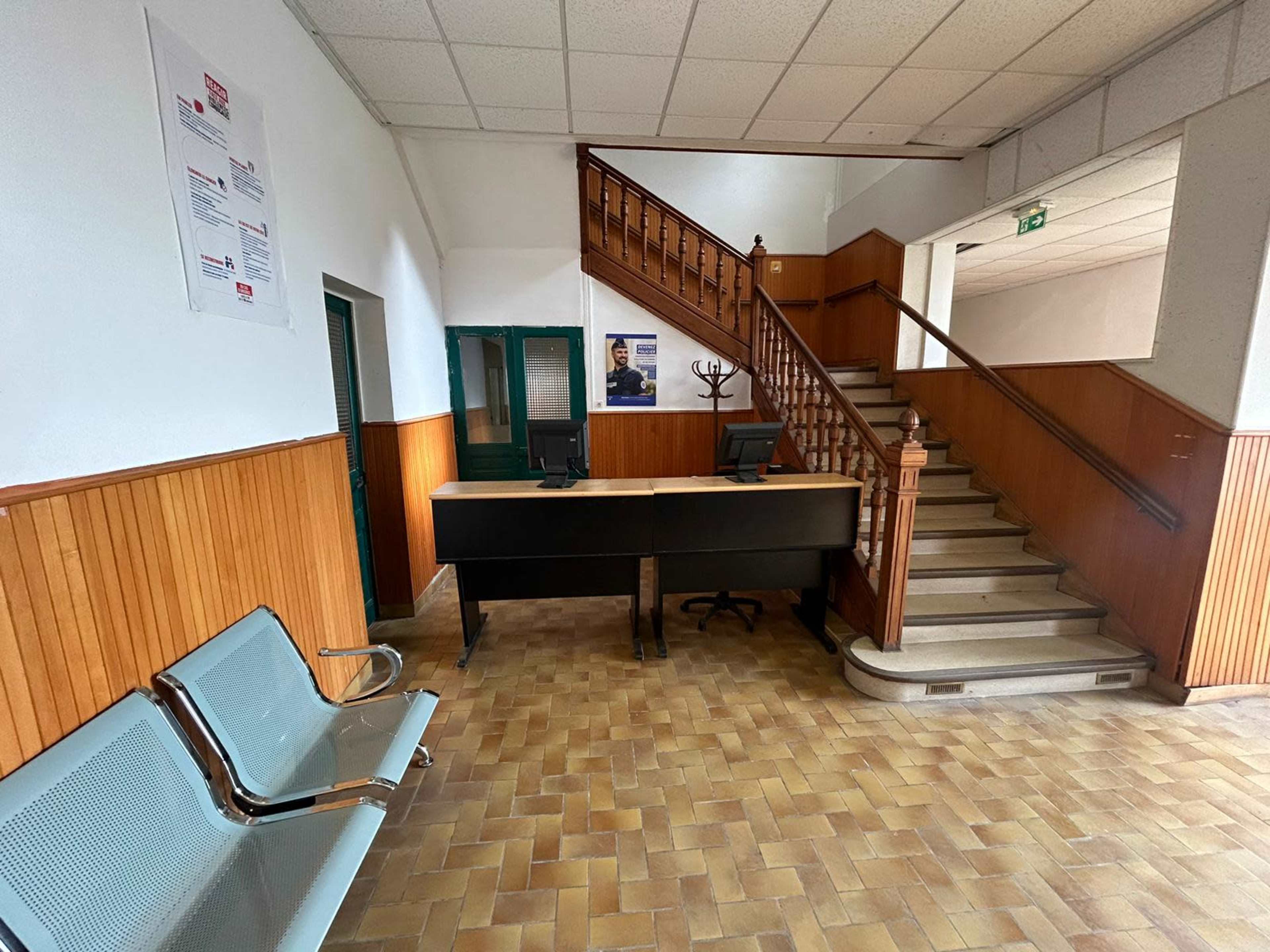 A spacious reception area with a front desk and a staircase leading to an upper level, flanked by seating and wooden paneling on the walls.