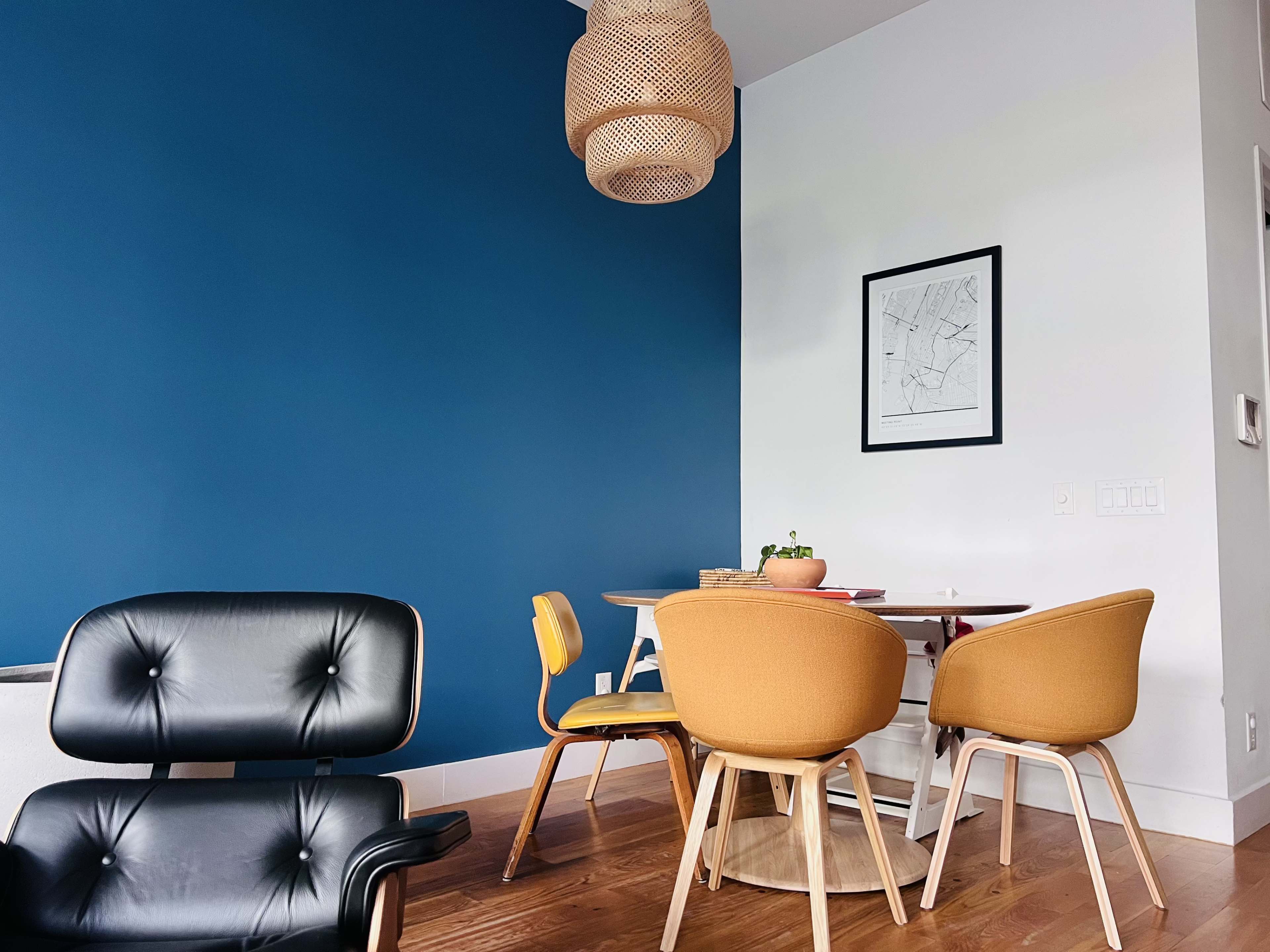 A dining area with a blue wall, a light fixture, a round table, and two yellow chairs alongside a black armchair.