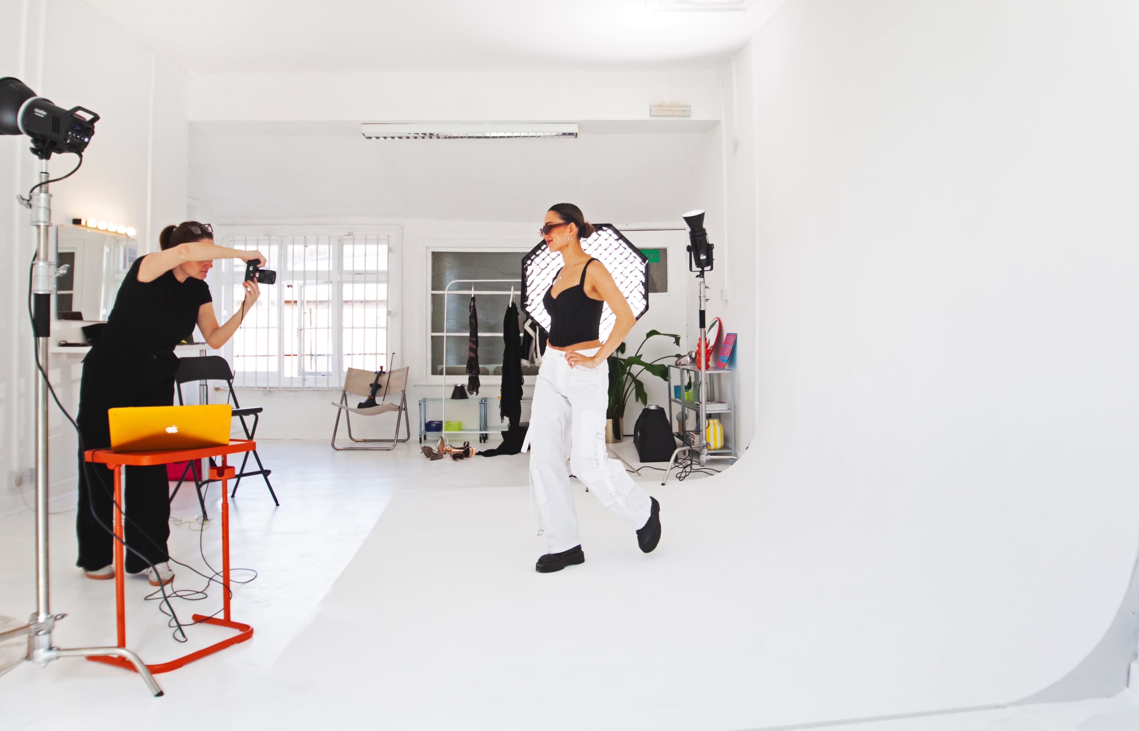 A model poses against a white backdrop while a photographer captures images in a studio setting.