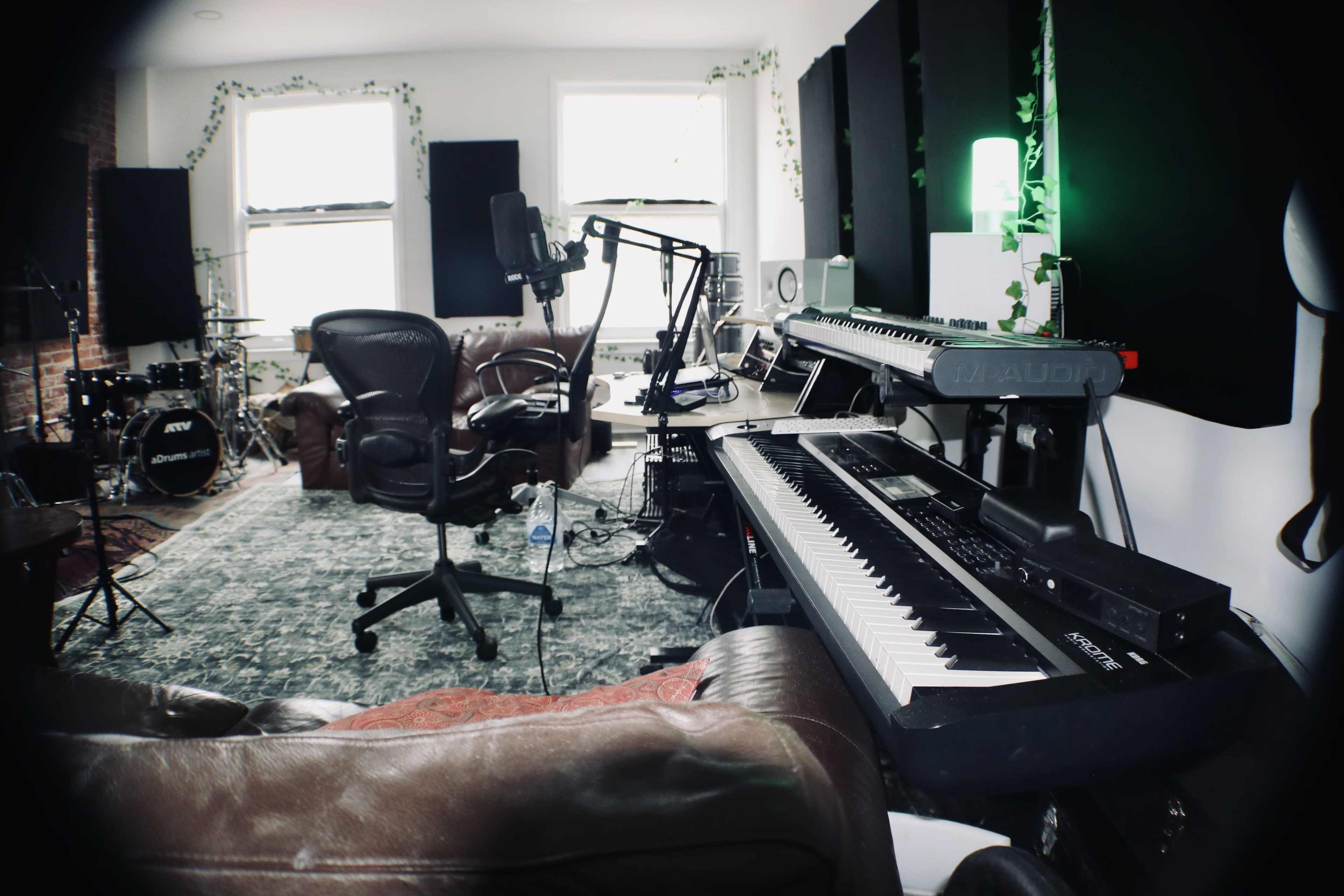 The image shows a music studio setup with musical instruments, a microphone on a stand, and seating arranged in a well-lit room.