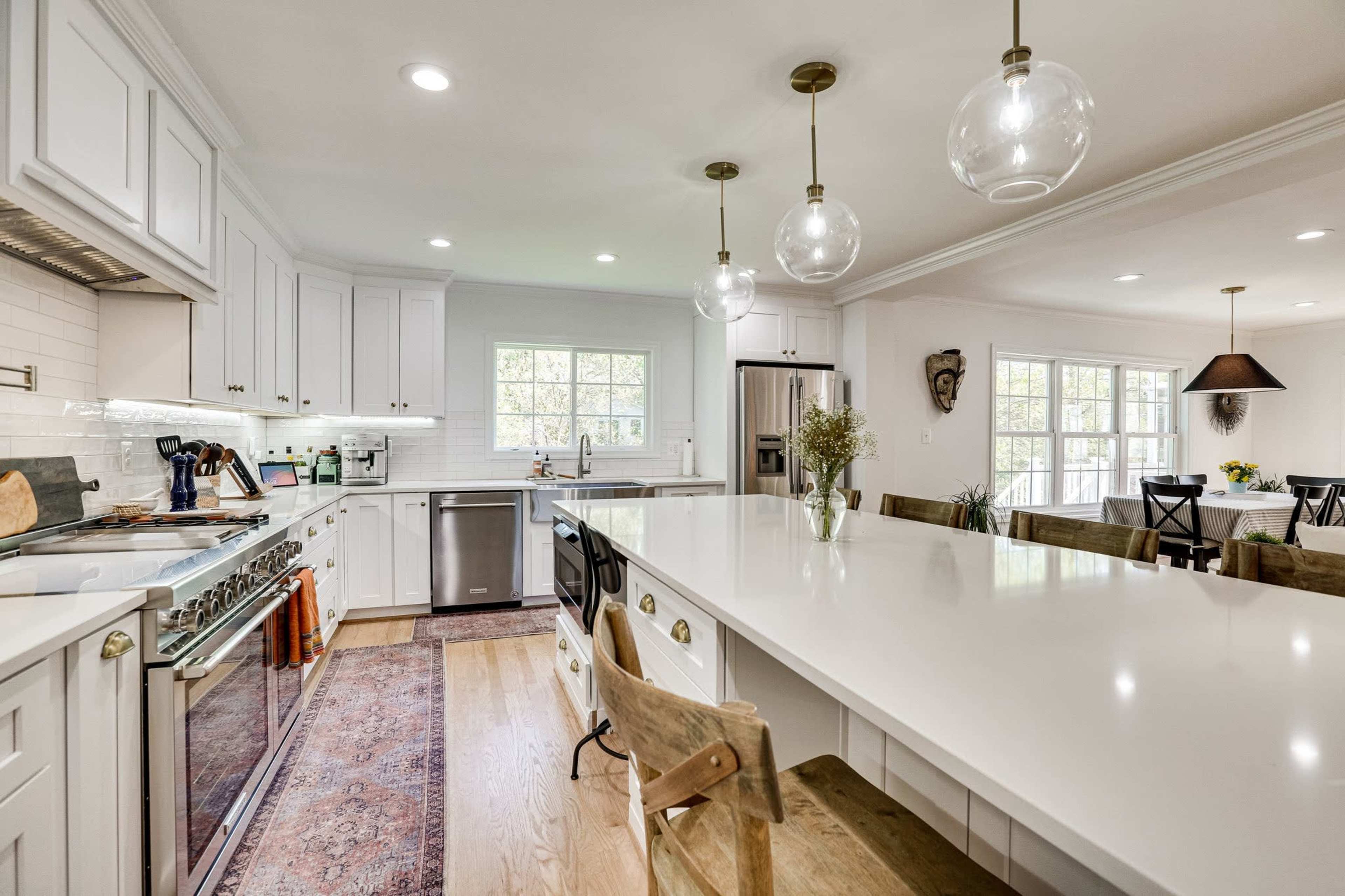 The image shows a modern kitchen with white cabinets, a large island featuring a countertop, and pendant lighting hanging above it.