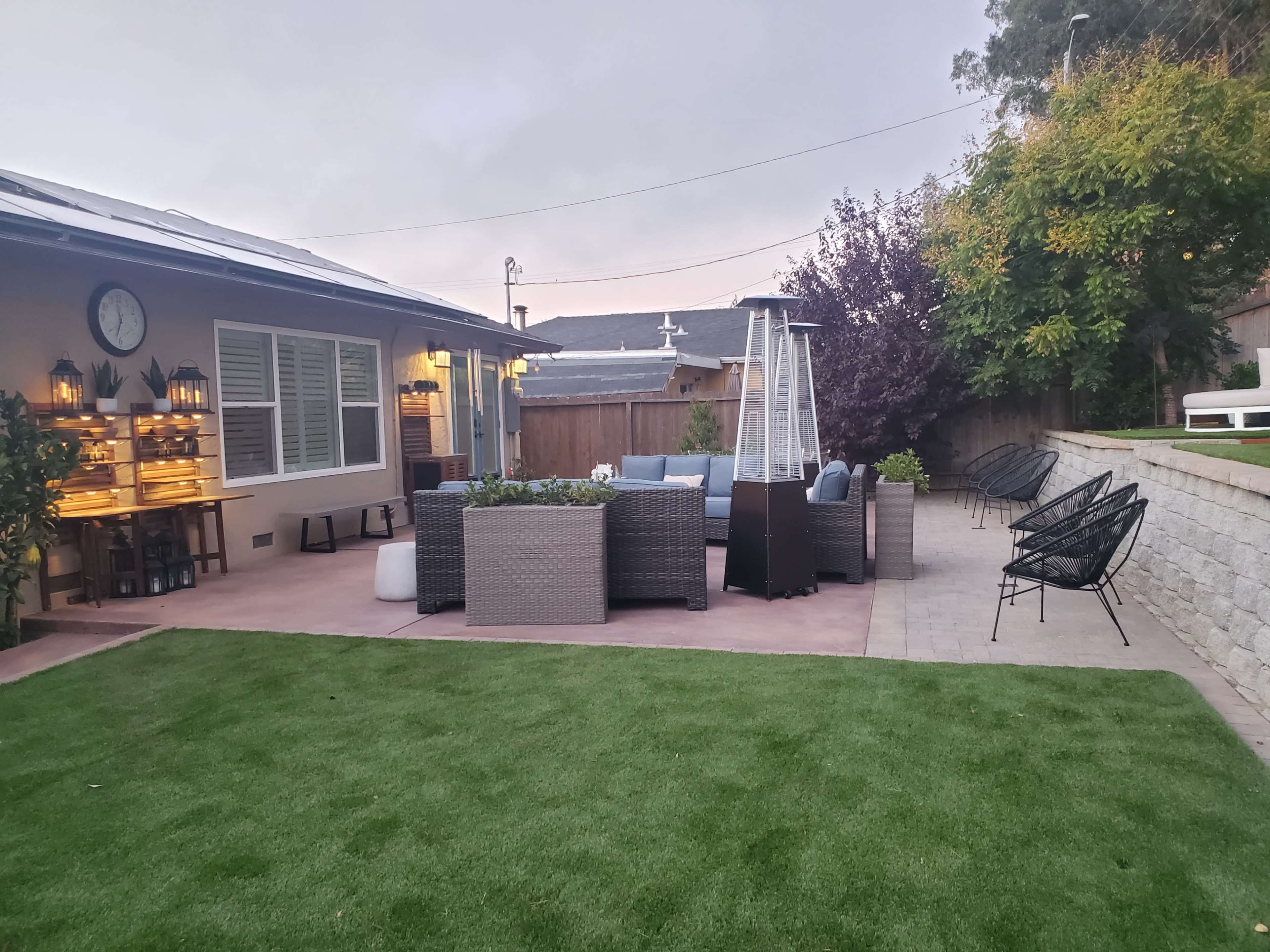 A patio area features outdoor seating, a gas heater, and landscaped grass beside a house.