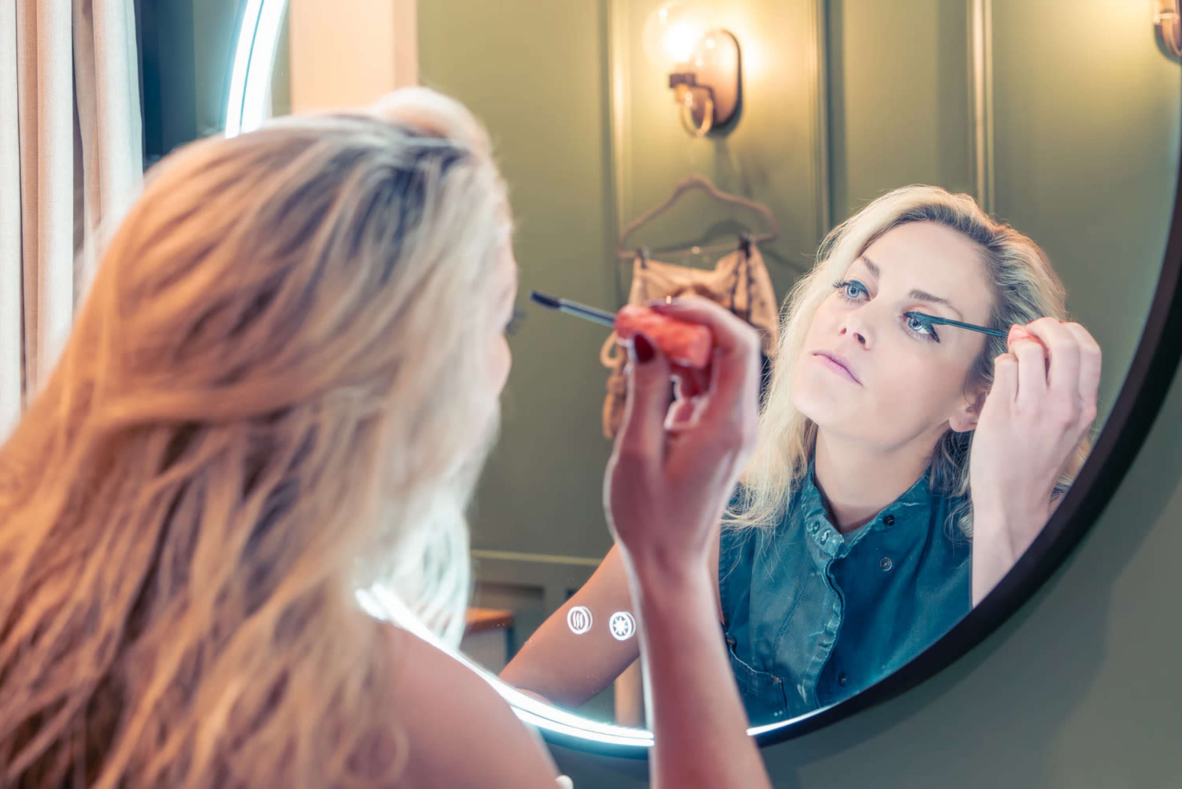 A woman applies mascara while looking into a circular mirror.