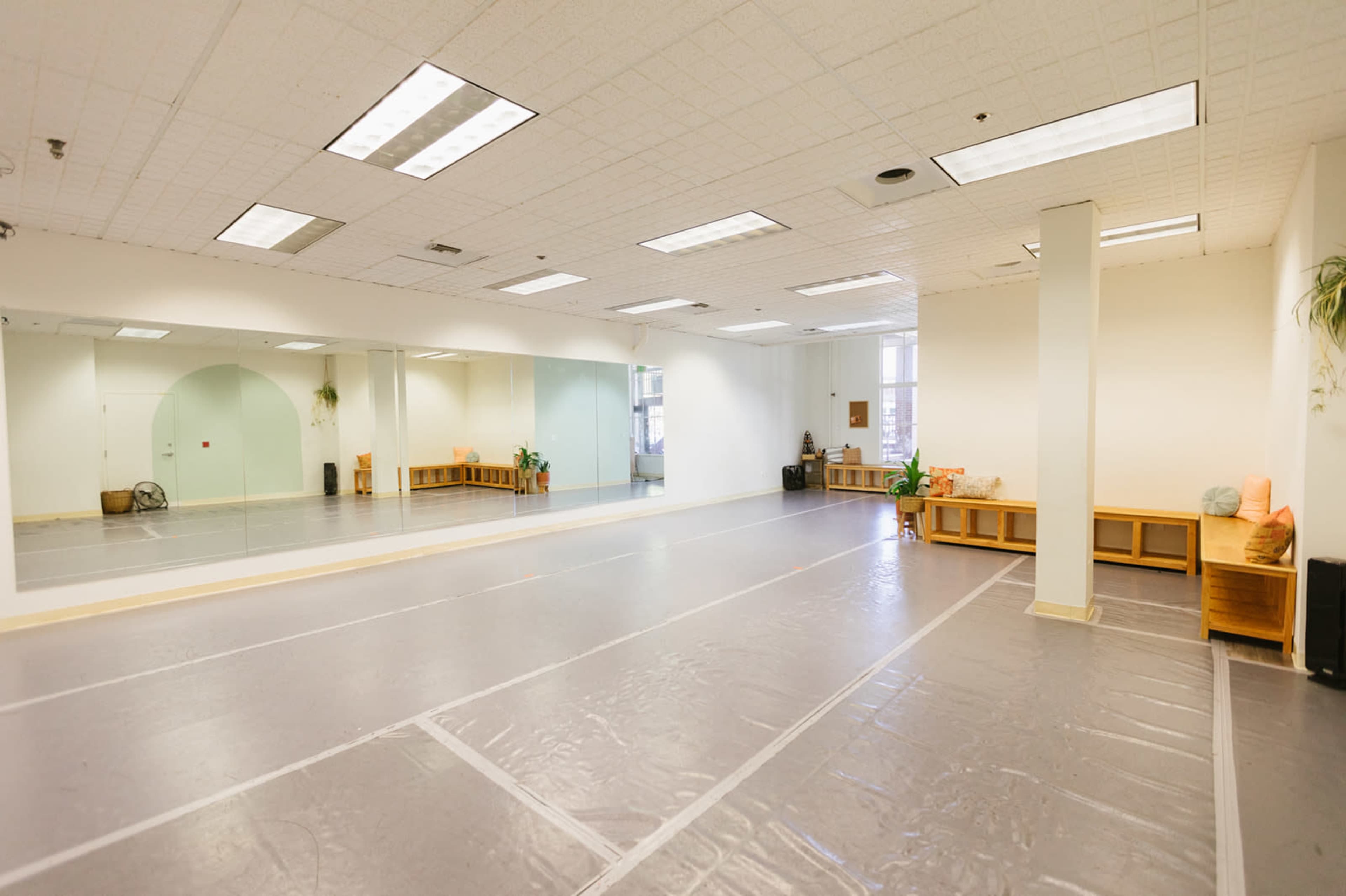 A spacious, empty studio with a mirrored wall, hardwood floors, and soft lighting.