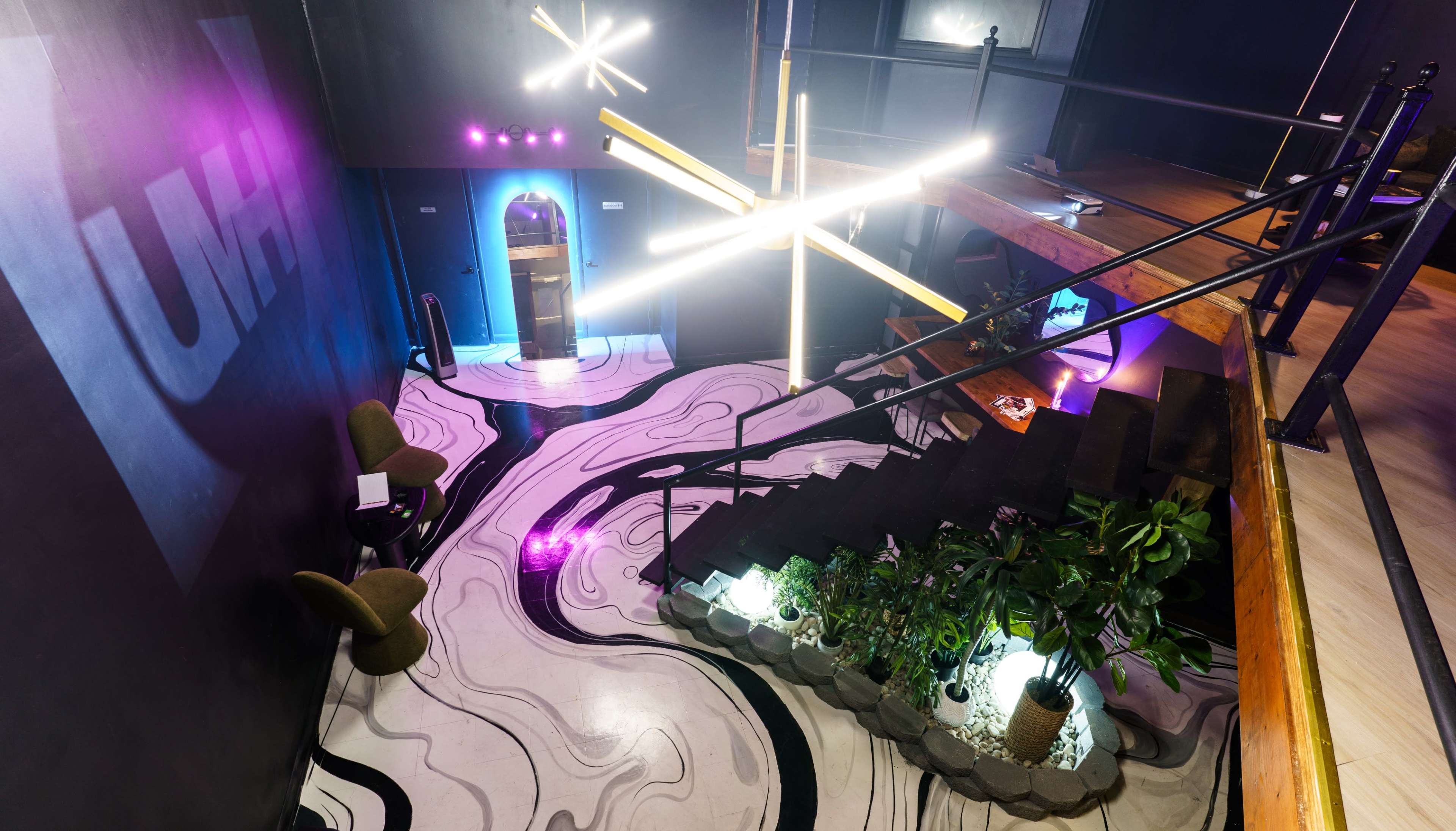 The image shows a modern interior space with a unique patterned floor, illuminated by geometric light fixtures, and featuring plants and furniture.