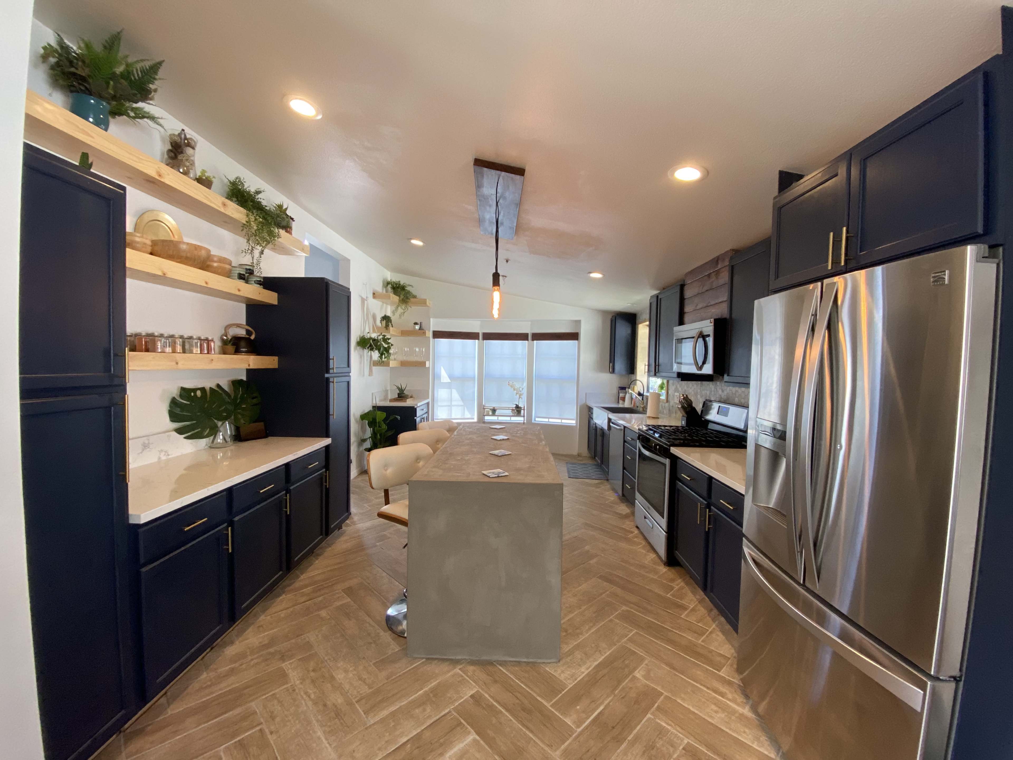 A modern kitchen with dark navy cabinetry, a central island with a gray countertop, and open shelving adorned with decorative items and plants.