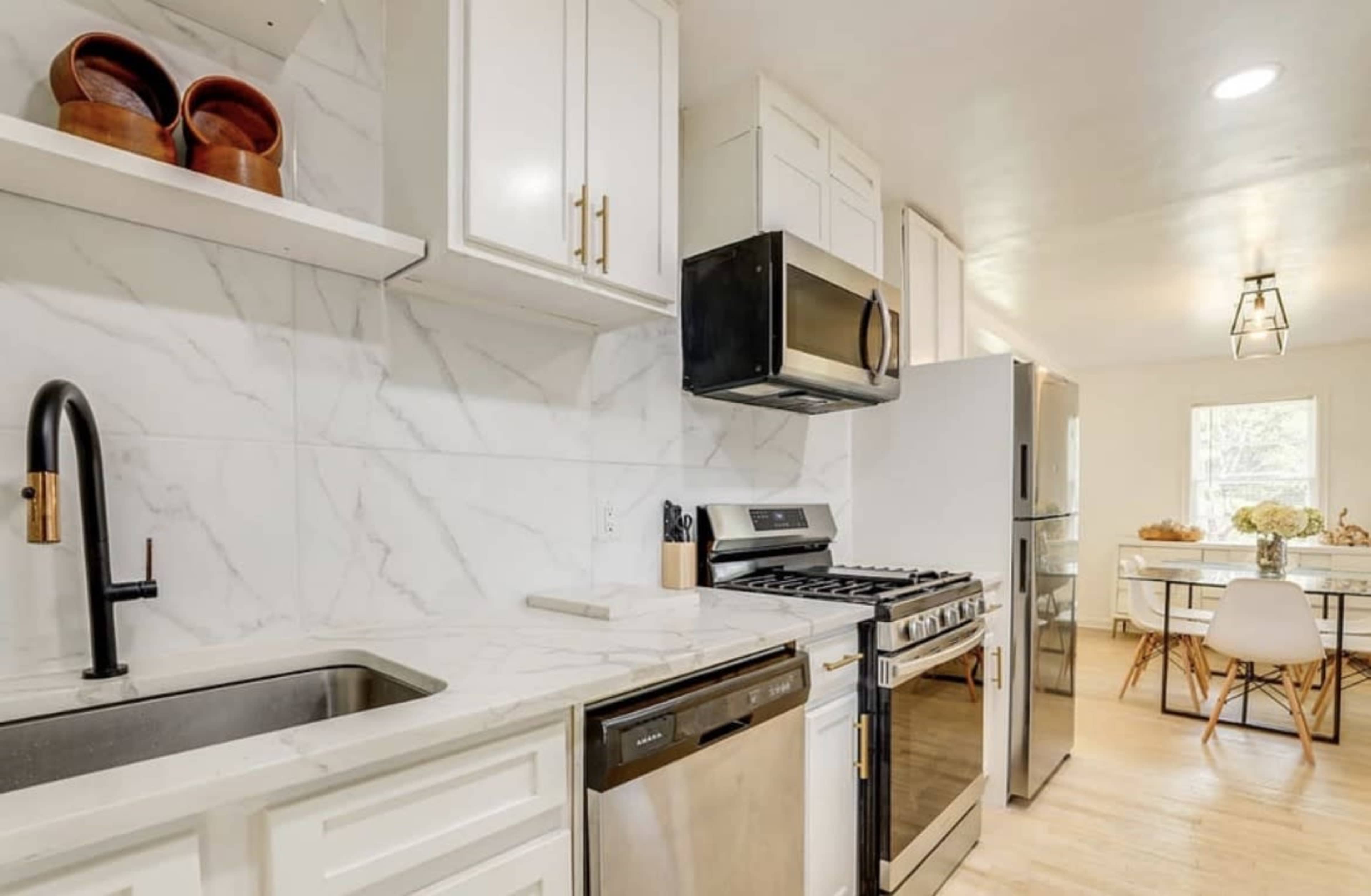 The image shows a modern kitchen featuring white cabinetry, stainless steel appliances, and a marble backsplash.
