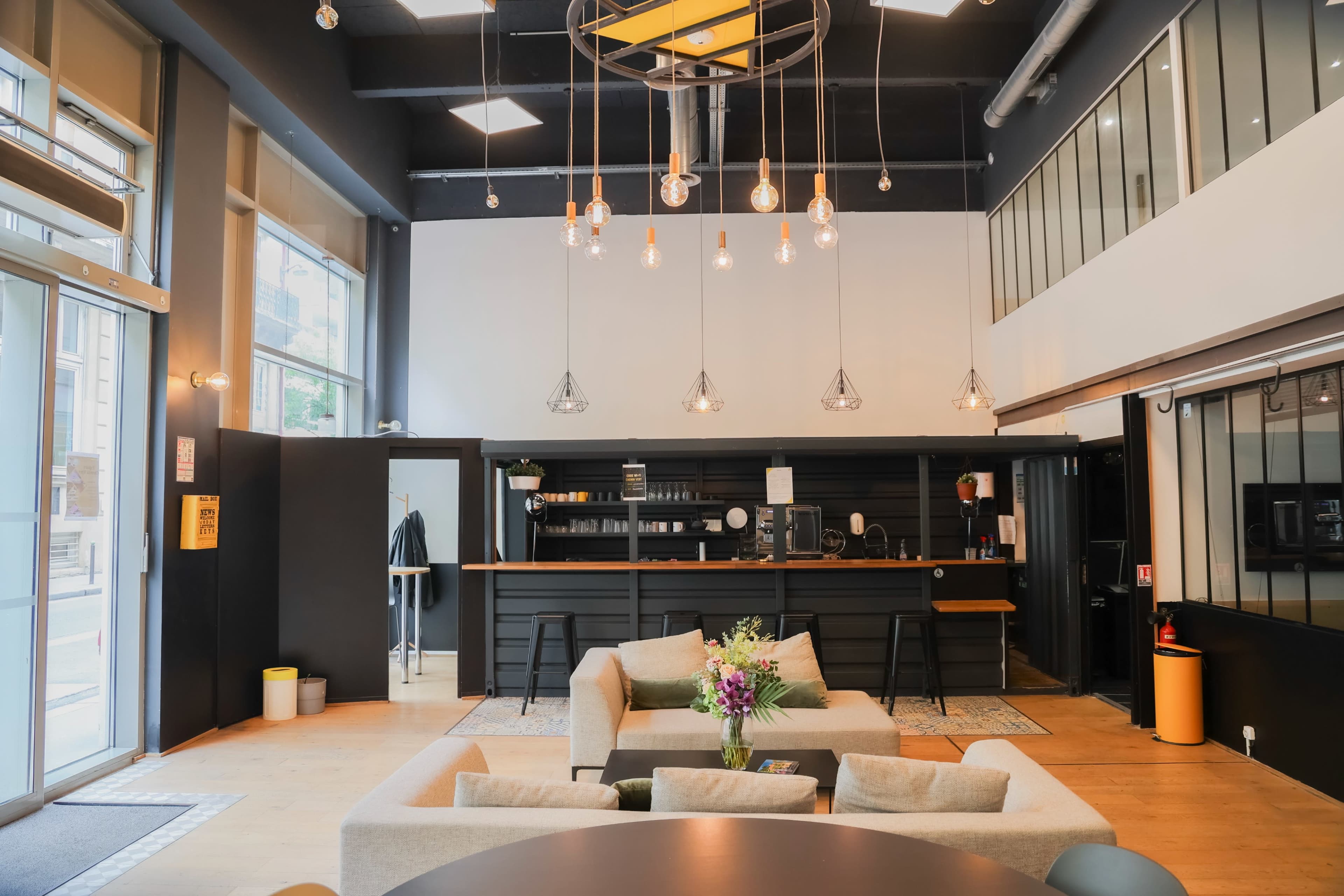 The image shows a modern interior of a lounge area featuring a bar, plush seating, and decorative lighting.