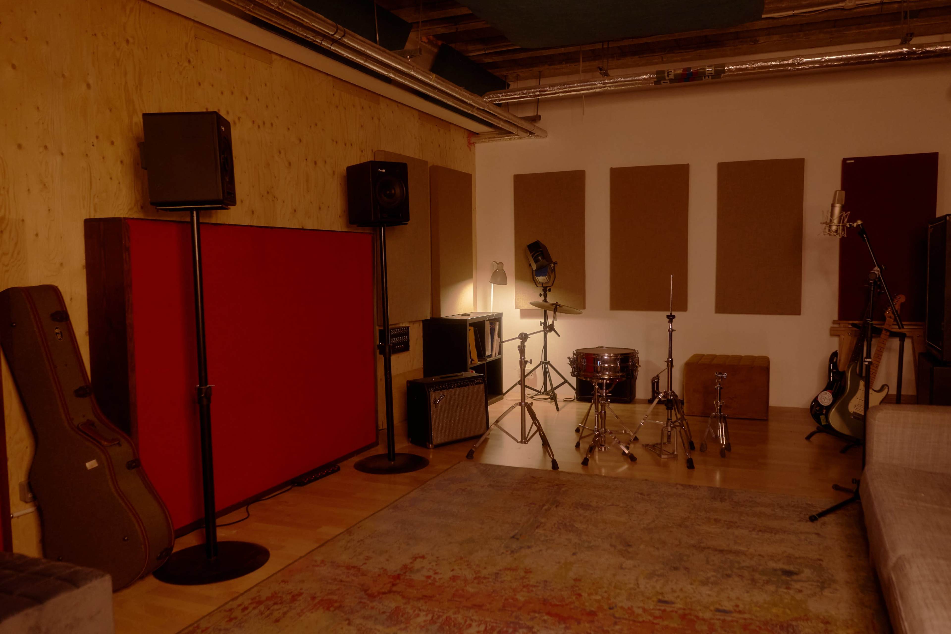 The image shows a music studio featuring various instruments, microphones, and sound equipment arranged around a vibrant red backdrop.