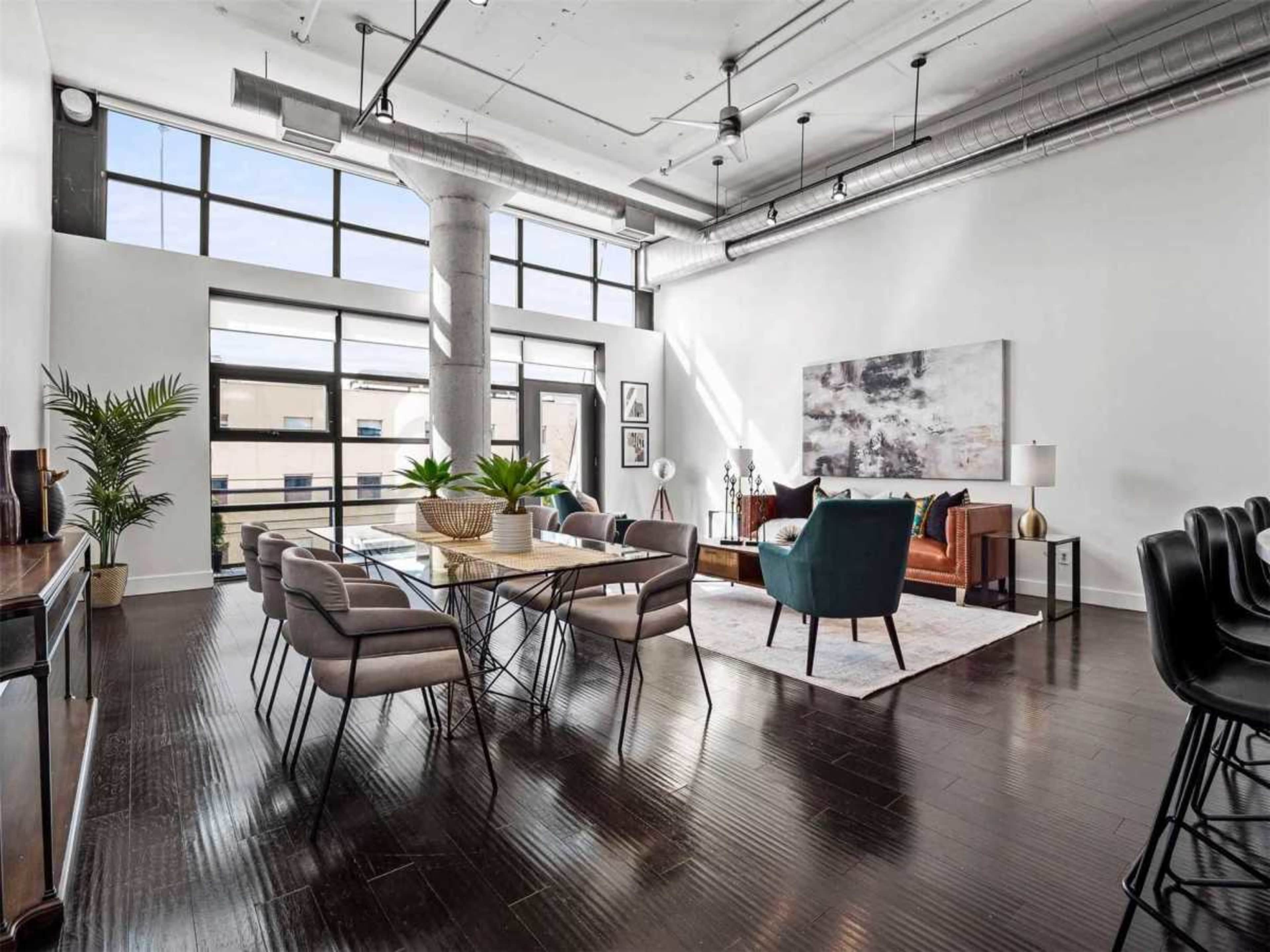 The image shows a modern open-concept living and dining area with a large table, chairs, and a sitting area featuring a sofa and armchair.