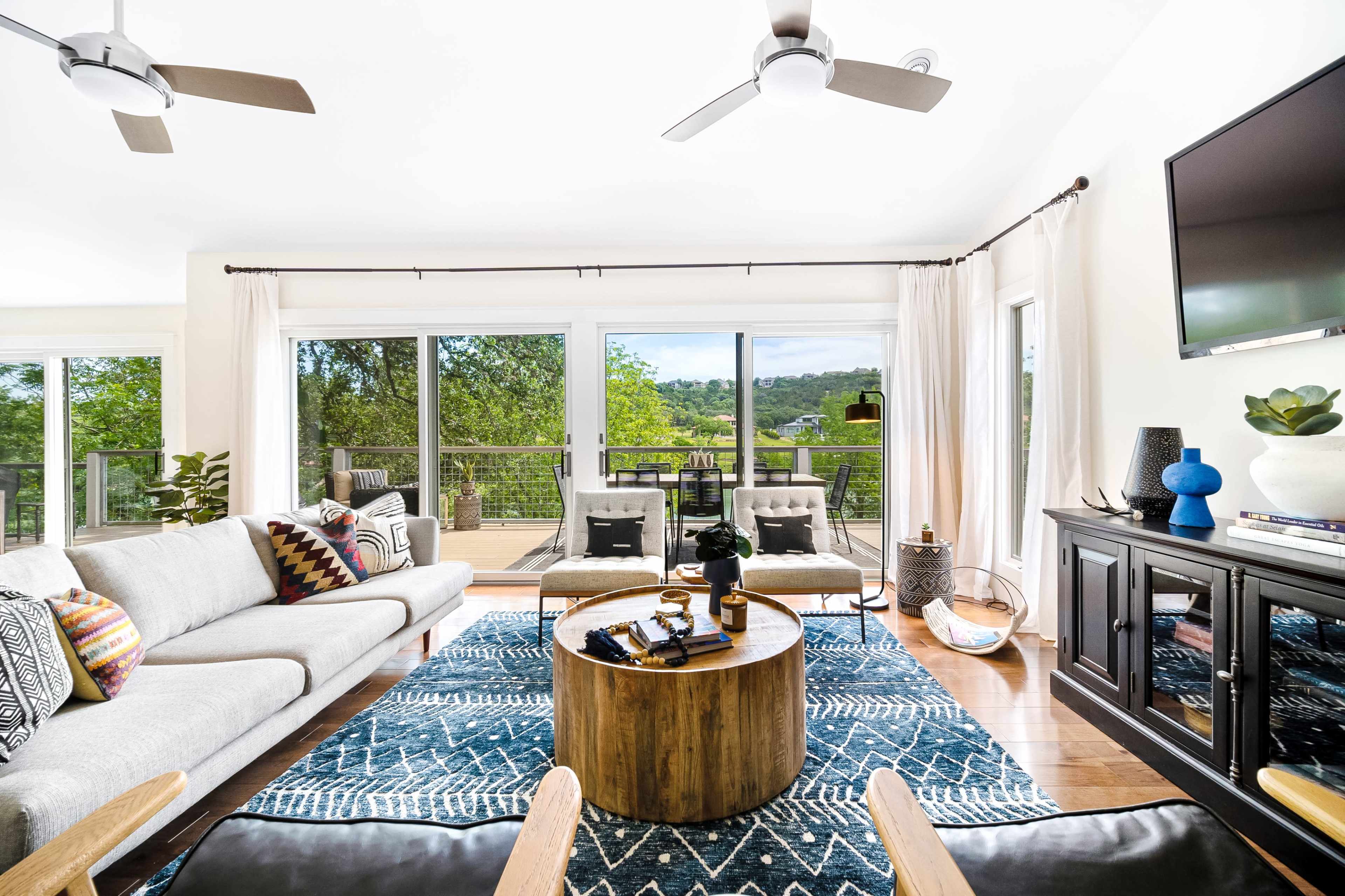 A contemporary living room with a large sectional sofa, a circular wooden coffee table, and sliding glass doors leading to a deck with outdoor furniture.