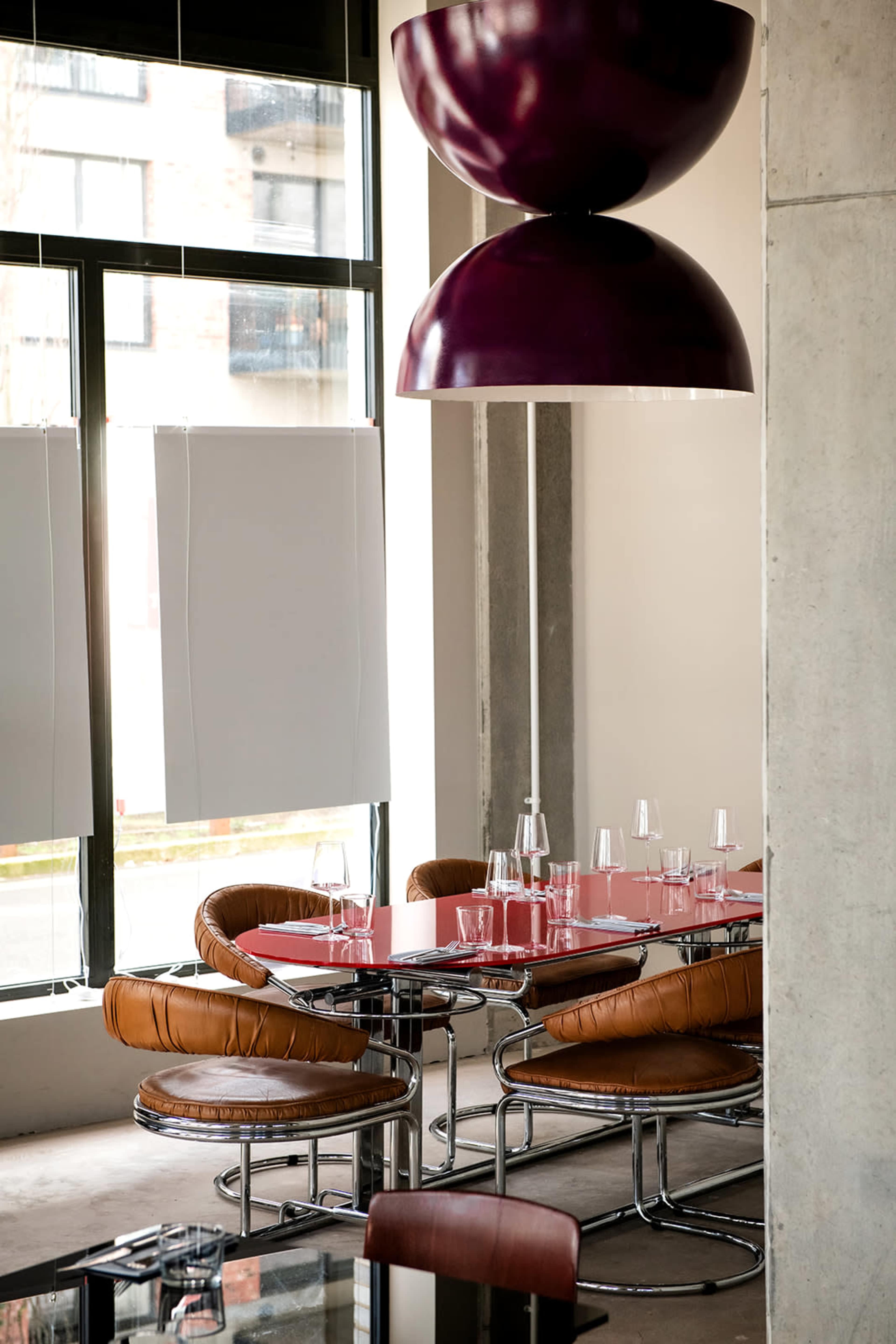 The image shows a modern dining area featuring a glass table surrounded by curved leather chairs, with a large, decorative pendant light overhead.