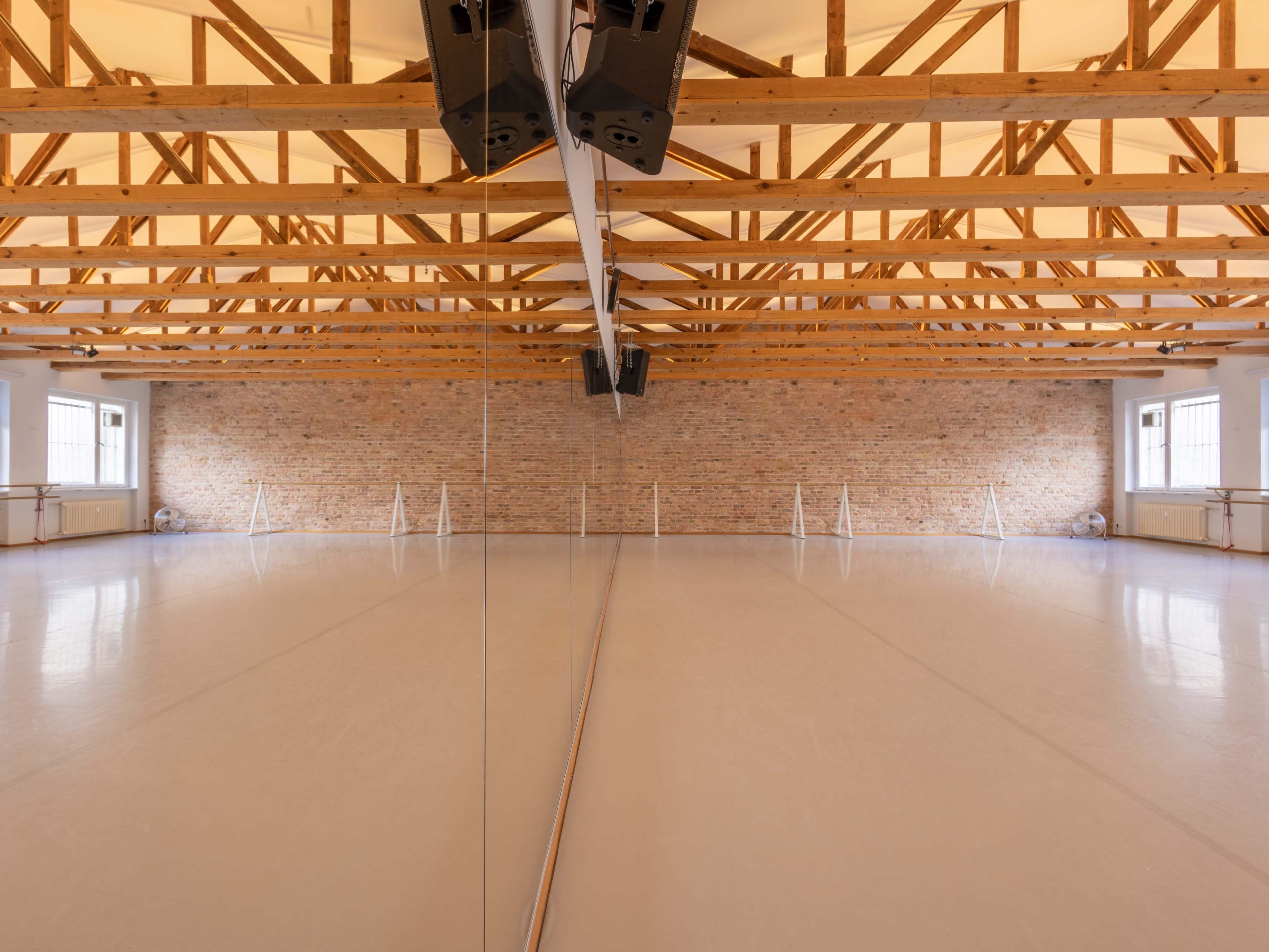 The image shows a spacious dance studio with wooden beams, brick walls, and a mirrored wall reflecting the smooth floor.