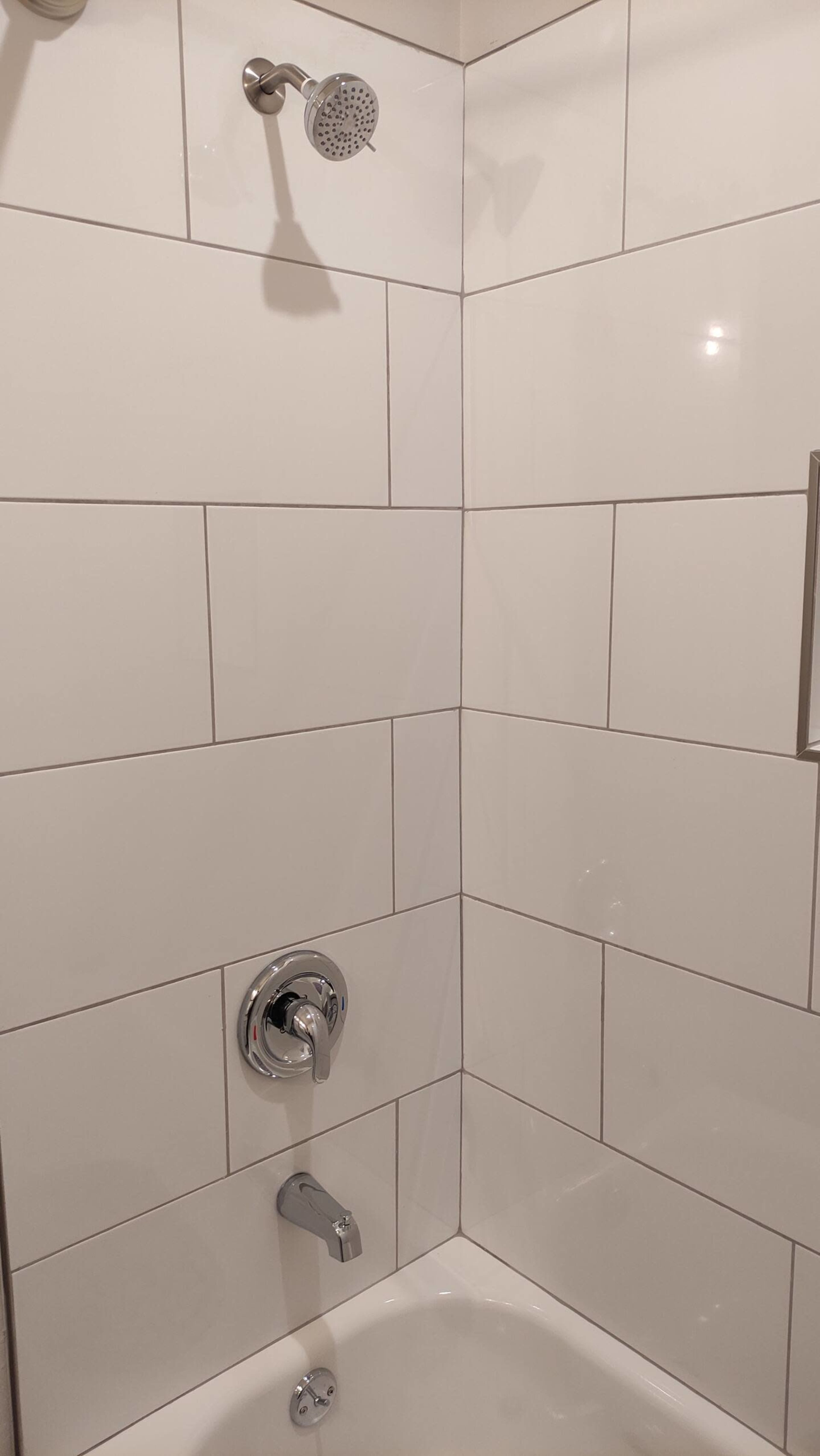 The image shows a tiled shower corner with a overhead showerhead, a wall-mounted faucet, and a water control handle.