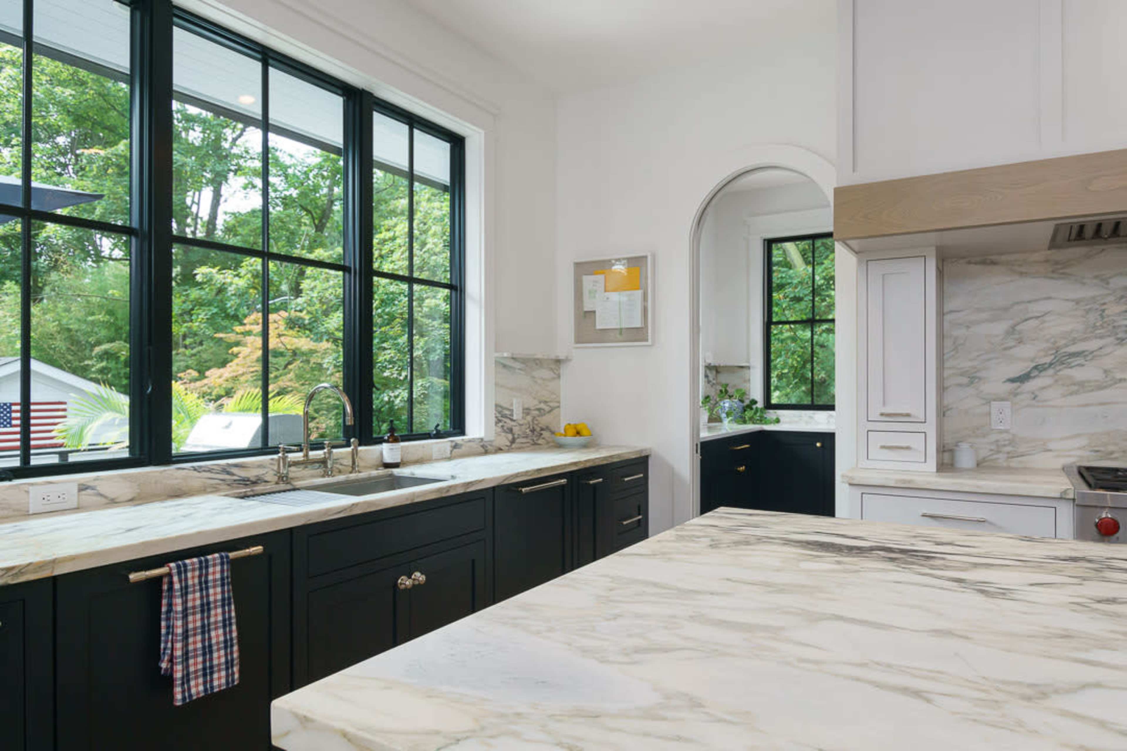 The kitchen features dark cabinetry, a large marble countertop, and expansive windows overlooking greenery.