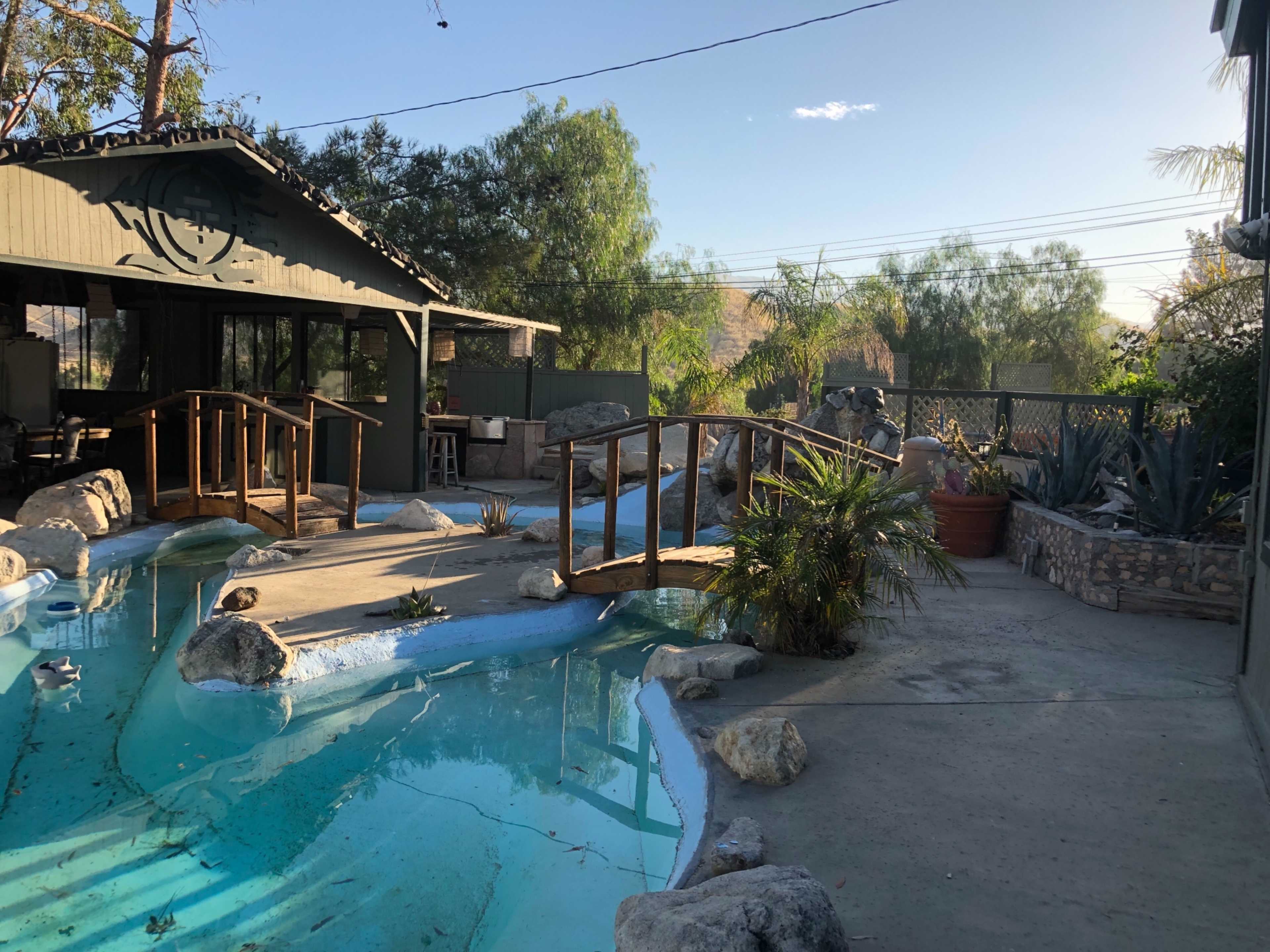 A backyard with a landscaped area featuring a small pool, wooden bridge, and surrounding greenery.