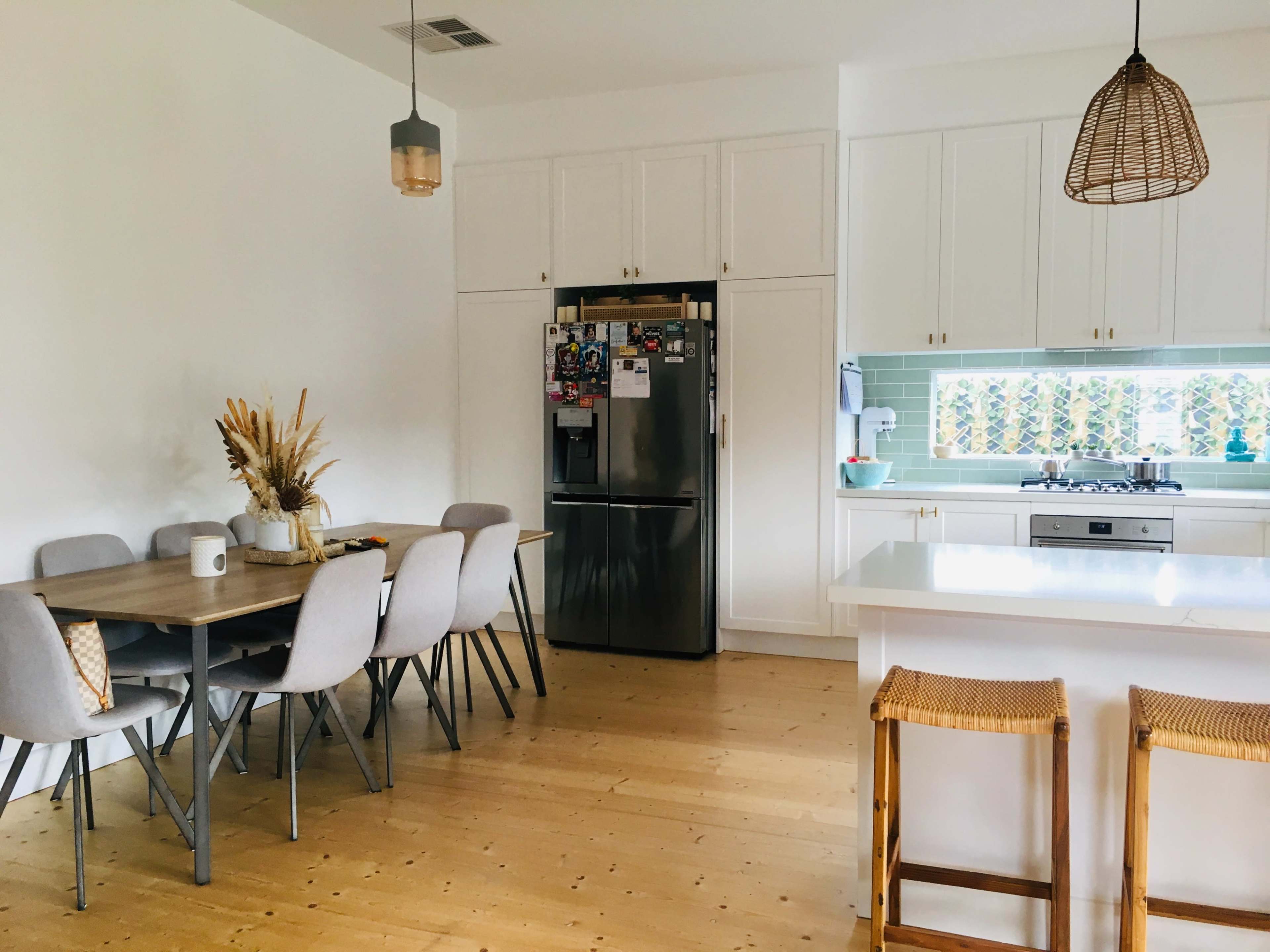 A kitchen and dining area features a table with six chairs, a refrigerator, and a stove, with natural light illuminating the space.