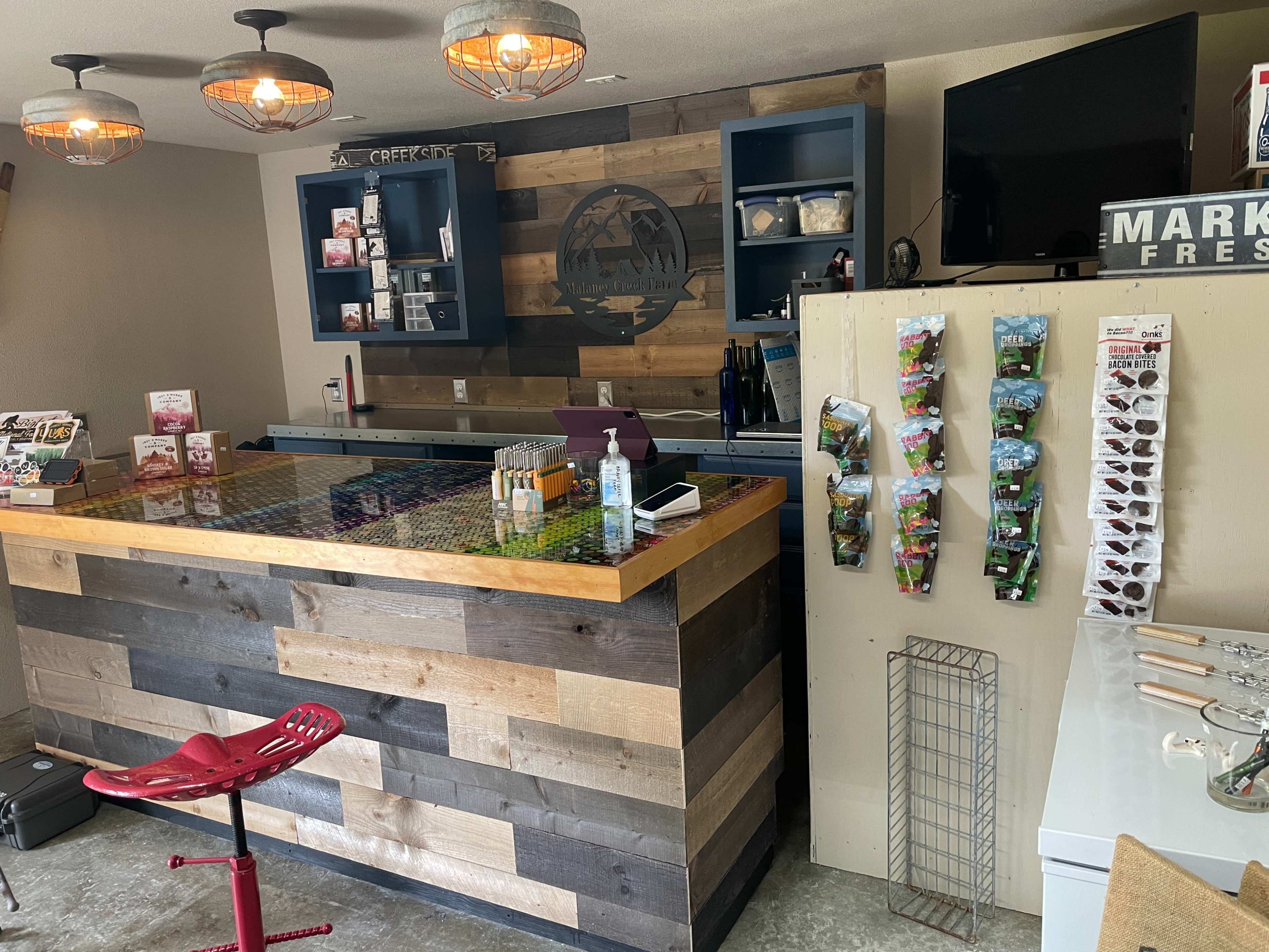A rustic counter area in a store, featuring a wooden design, a television on the wall, and displayed merchandise on the sides.