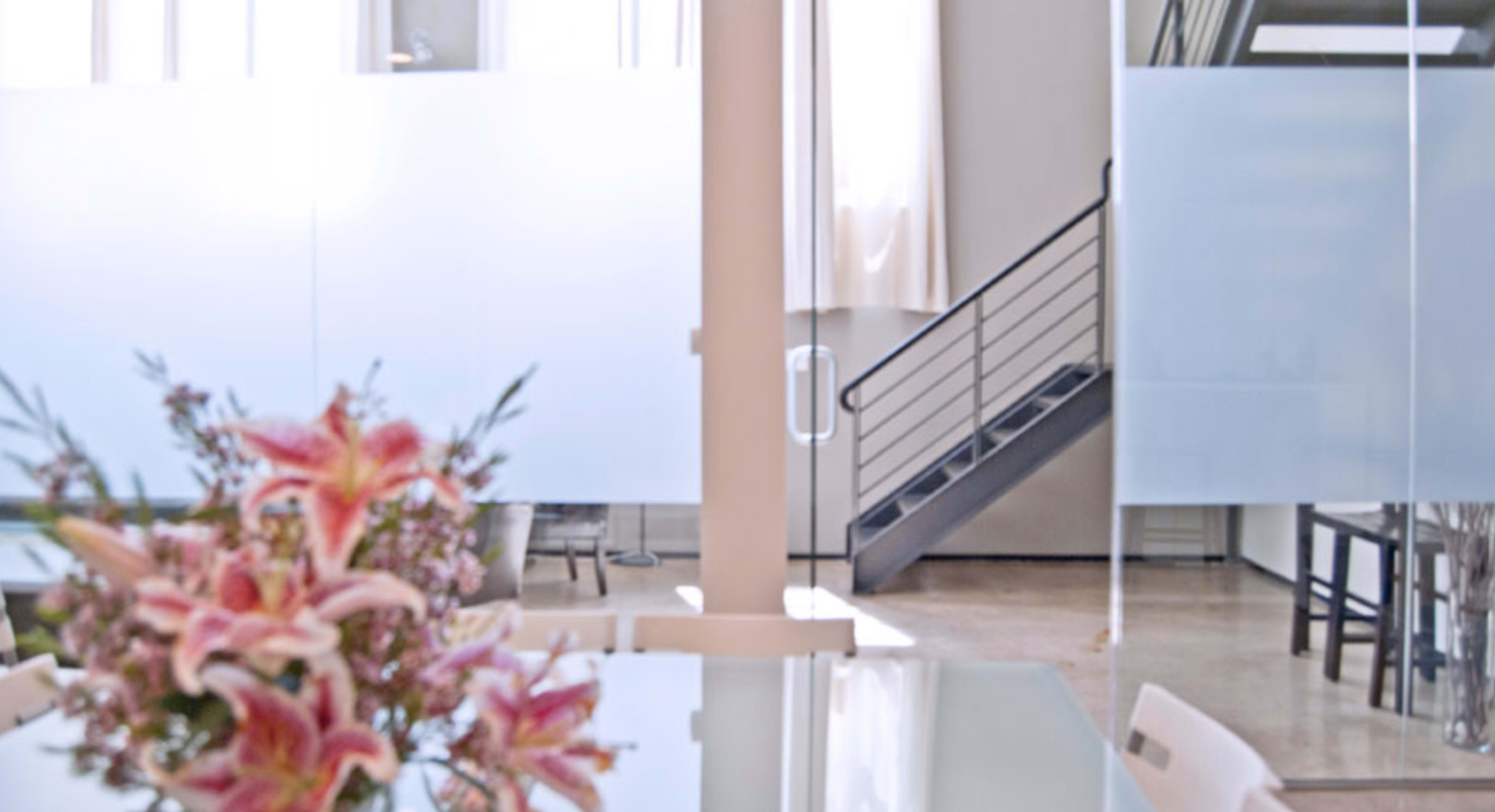 A modern office interior with a glass partition, a staircase, and a table with a vase of flowers.