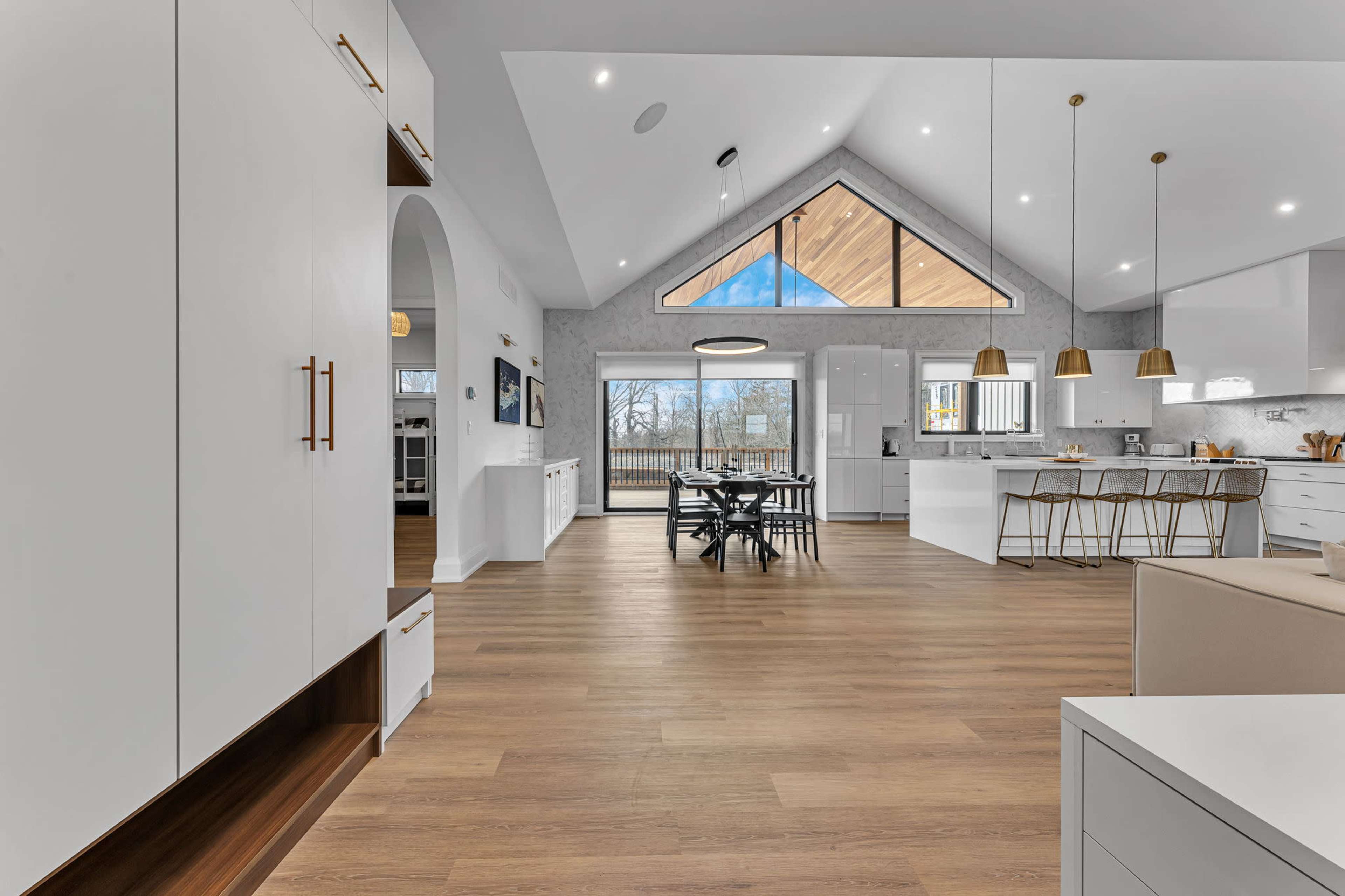 A modern kitchen and dining area with large windows, wooden flooring, and high ceilings featuring a triangular design.