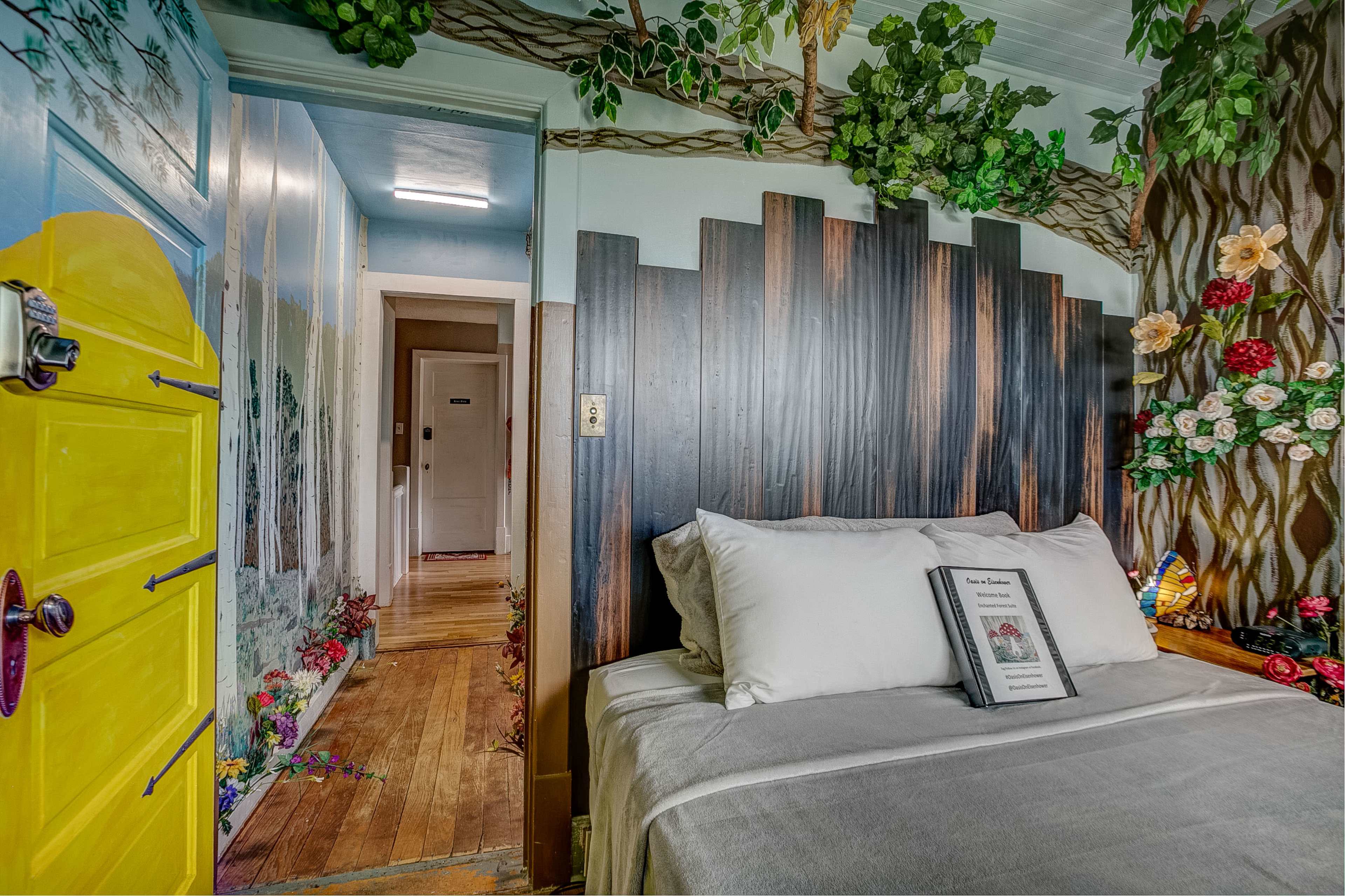 A cozy bedroom with a wooden headboard, floral decorations on the walls, and a brightly colored door leading to a hallway.