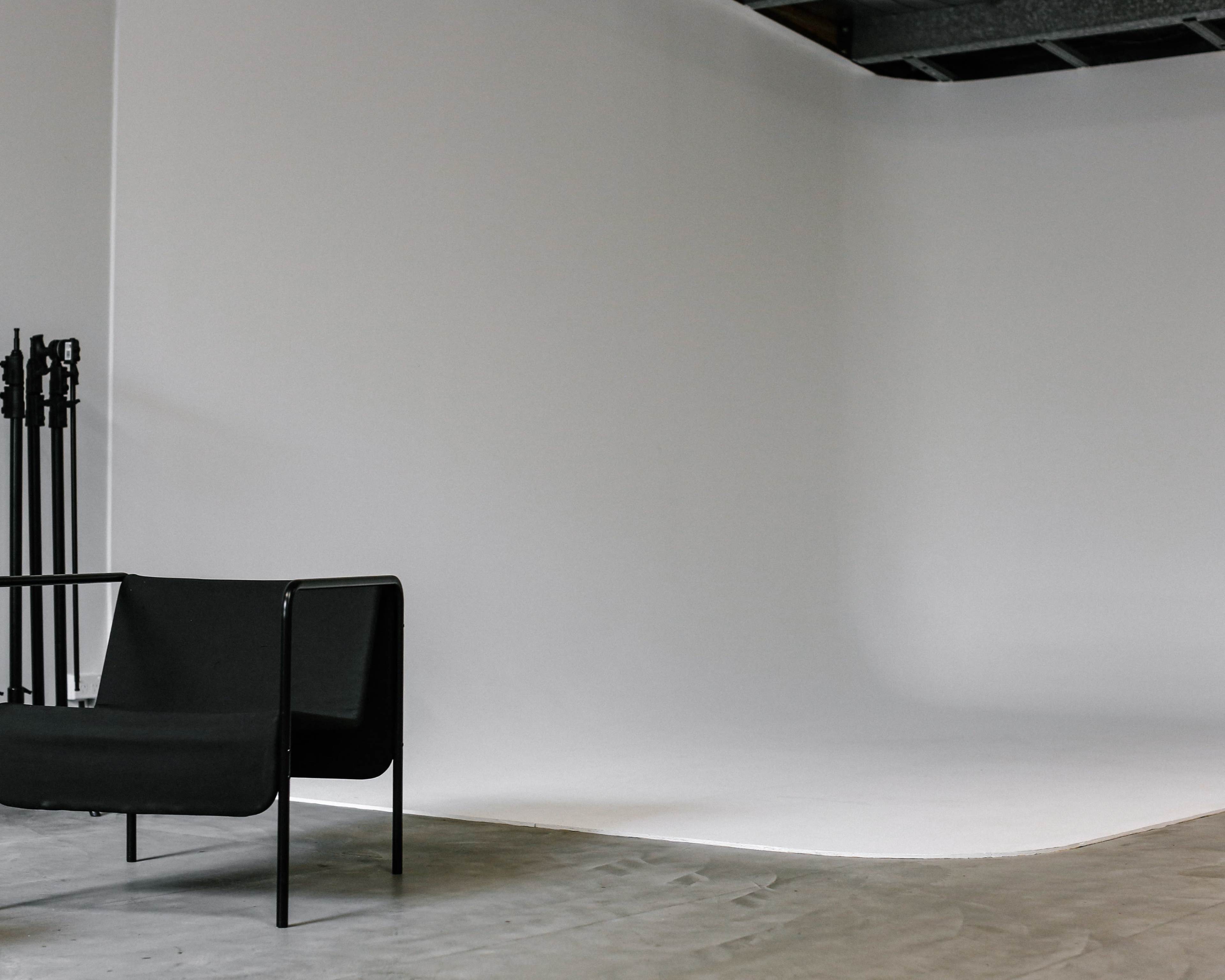 A black chair is positioned in front of a blank, white backdrop in a studio space.