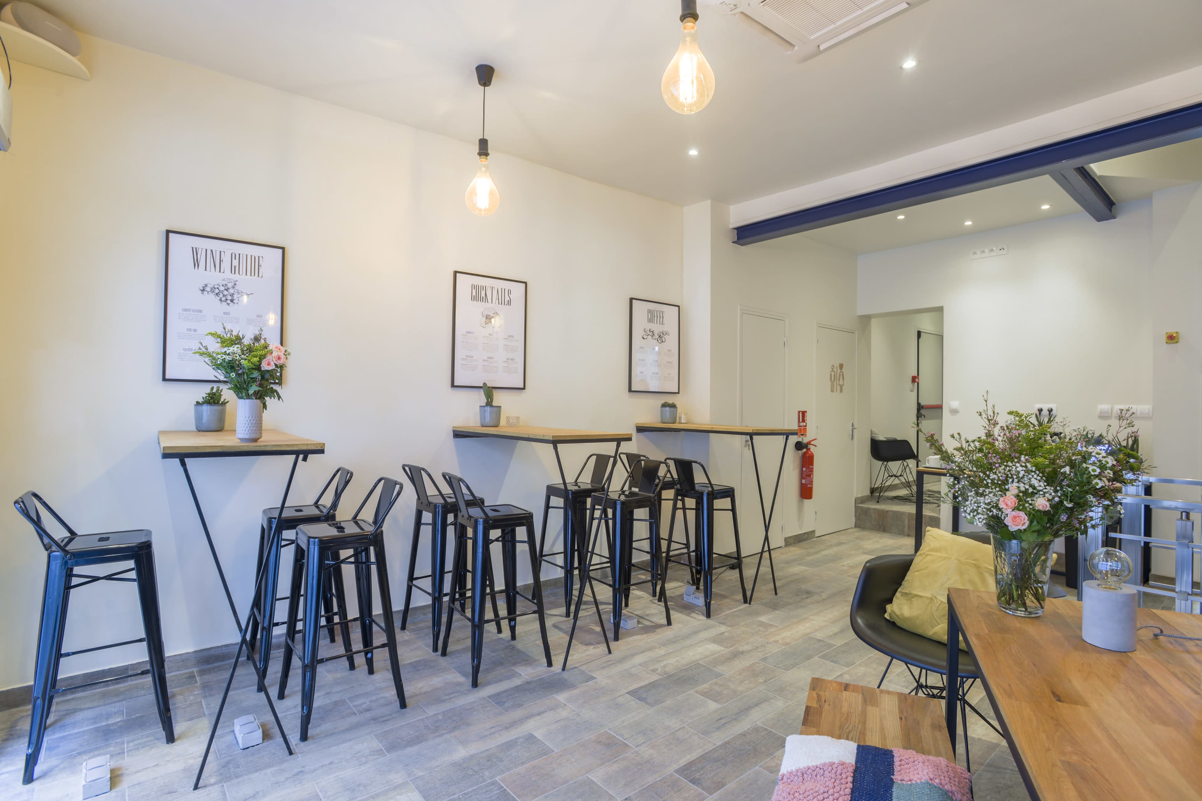 A modern café interior with high tables and stools, potted plants, and framed menus on the walls.