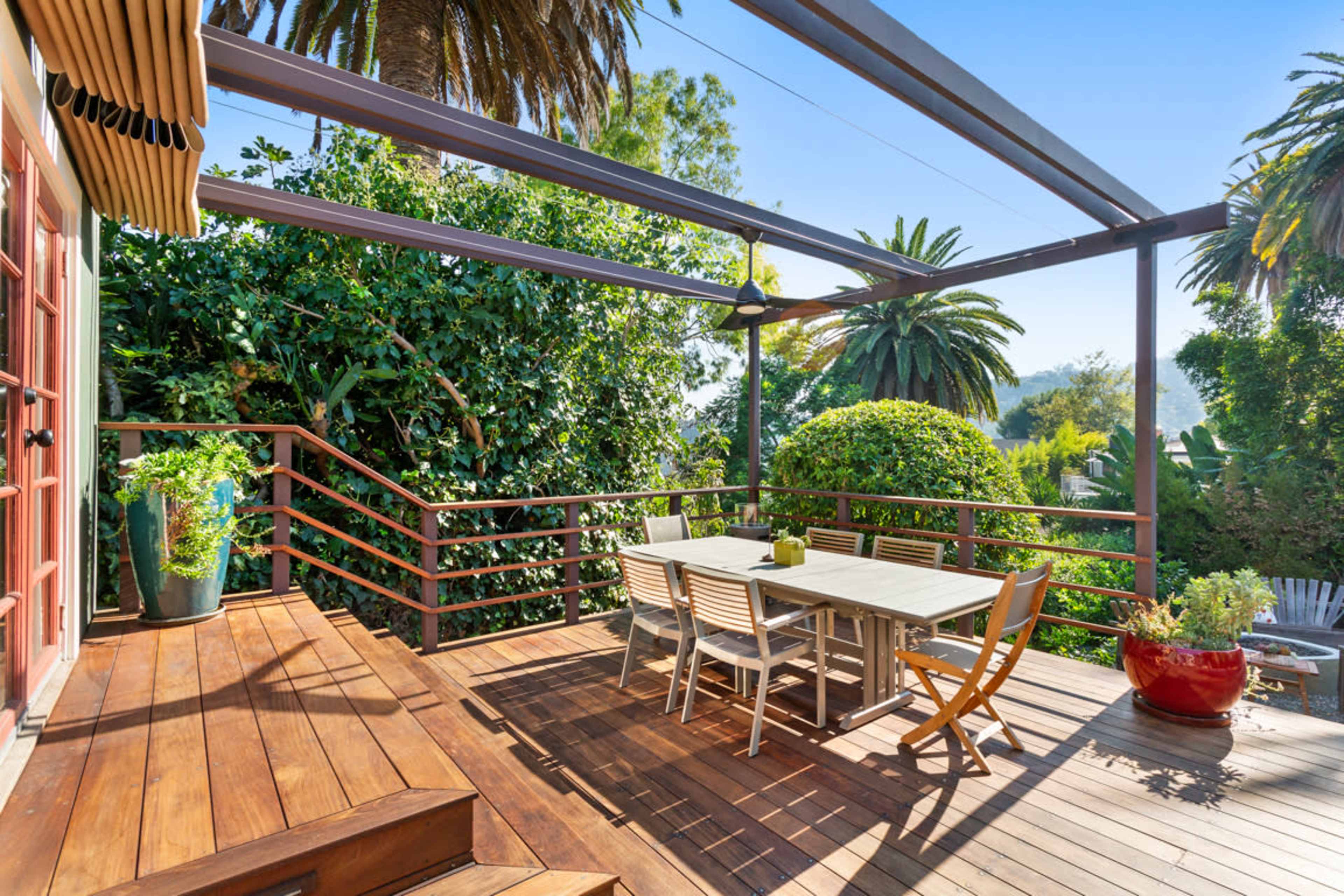 A spacious wooden deck with a dining table and chairs is surrounded by lush greenery and palm trees.