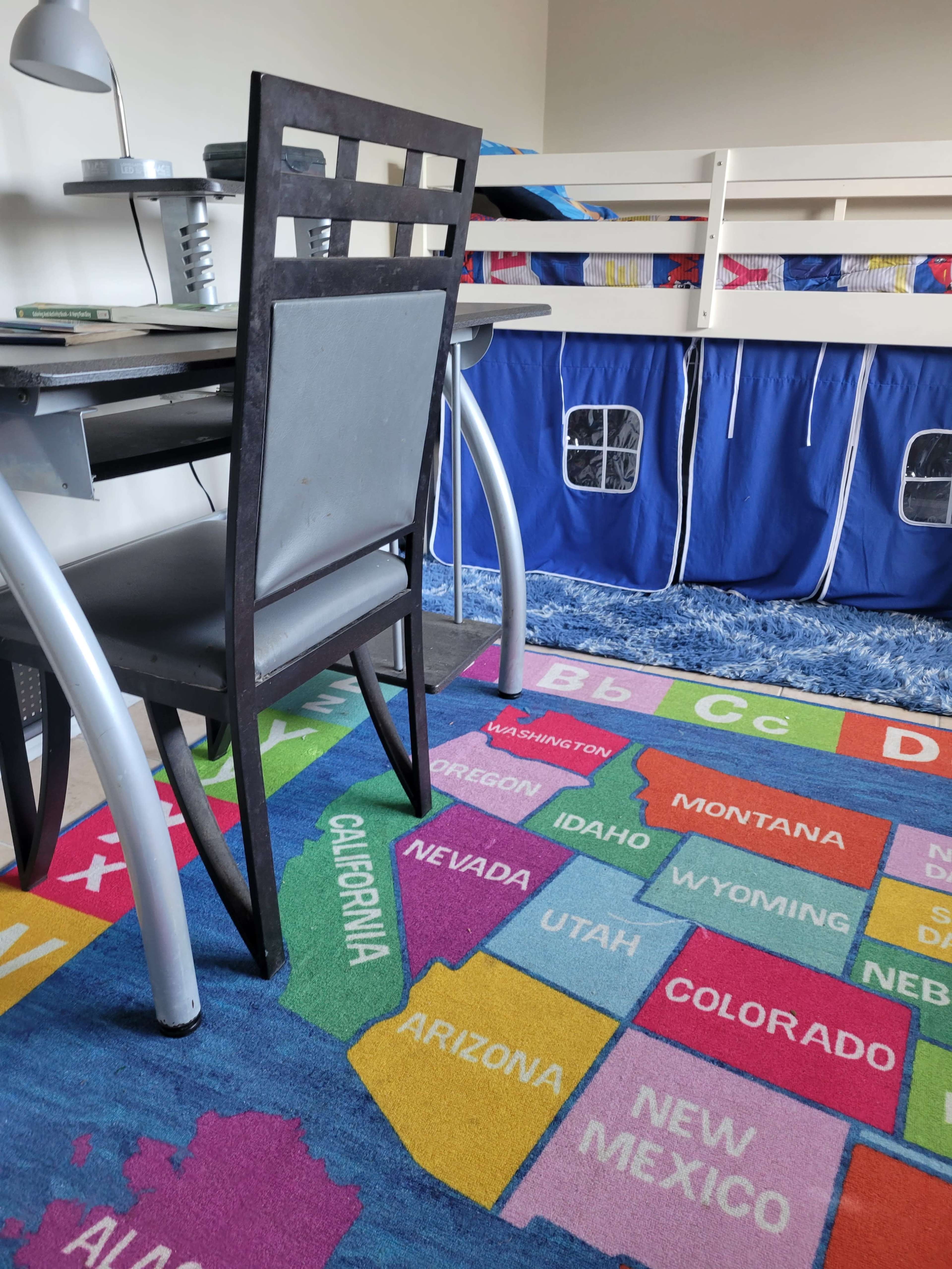 A children's bedroom with a colorful rug depicting a map of the United States, a desk and chair, and a bunk bed in the background.