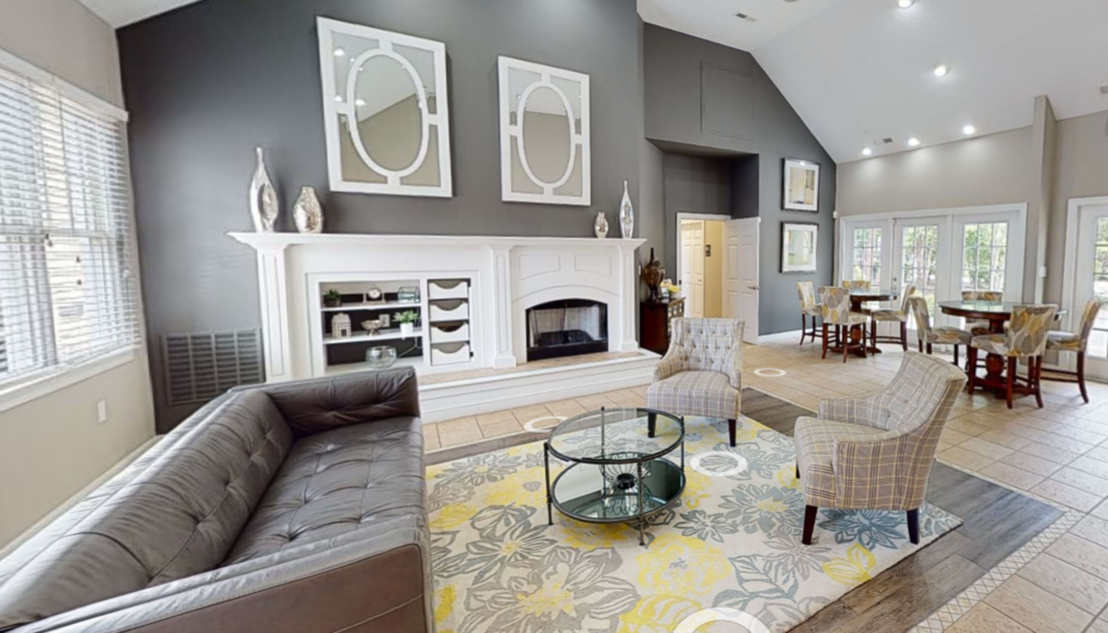 A modern living room features a dark gray accent wall, a fireplace with a white mantel, a patterned area rug, and seating arrangements with a glass coffee table.