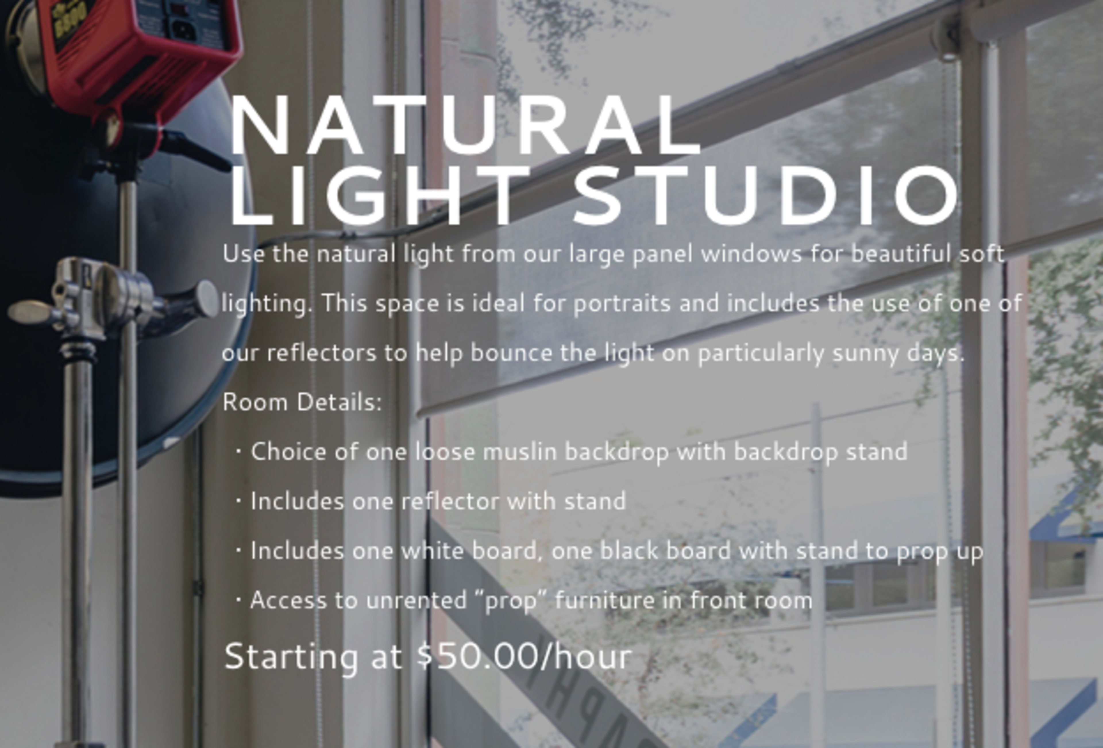 An indoor studio space with large windows, equipped for natural lighting with a backdrop stand and reflective equipment.