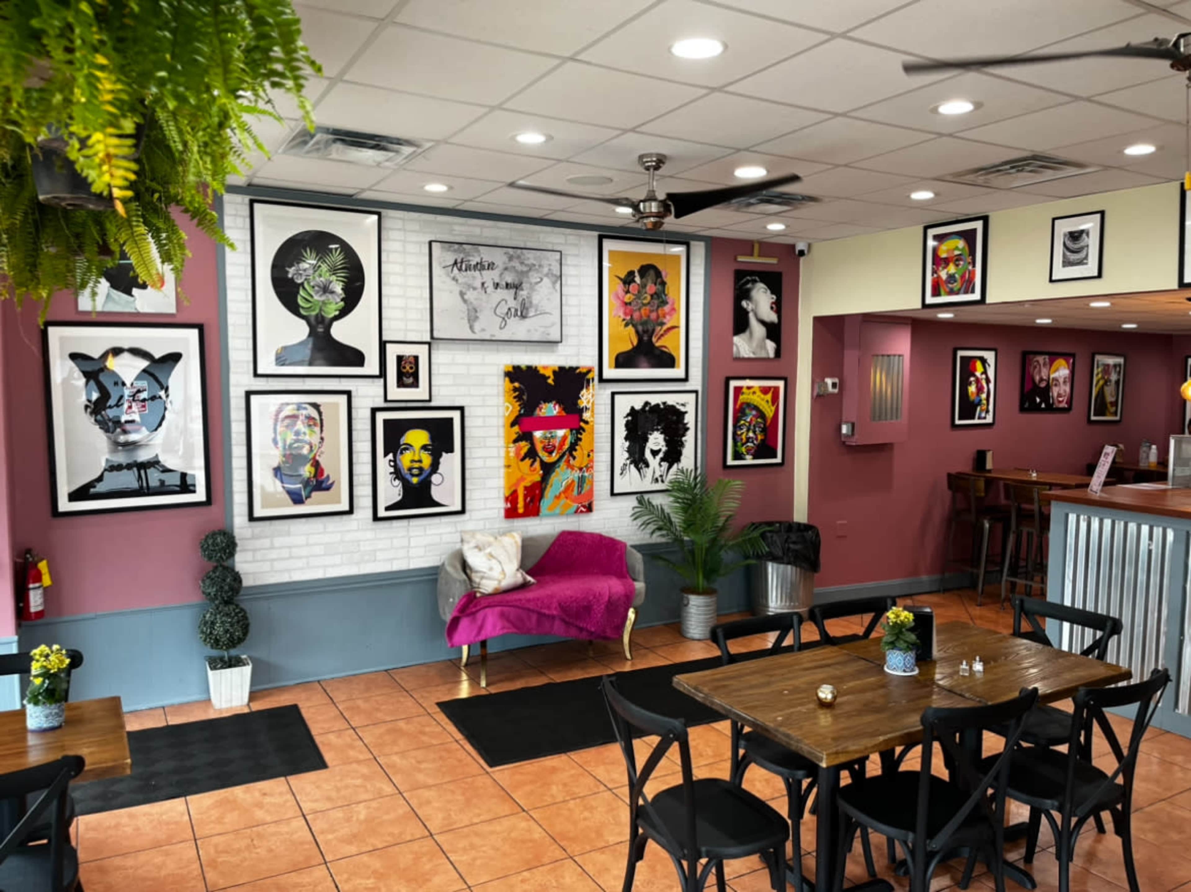 A vibrant cafe interior decorated with colorful portraits on the walls, a pink couch, and wooden tables for seating.