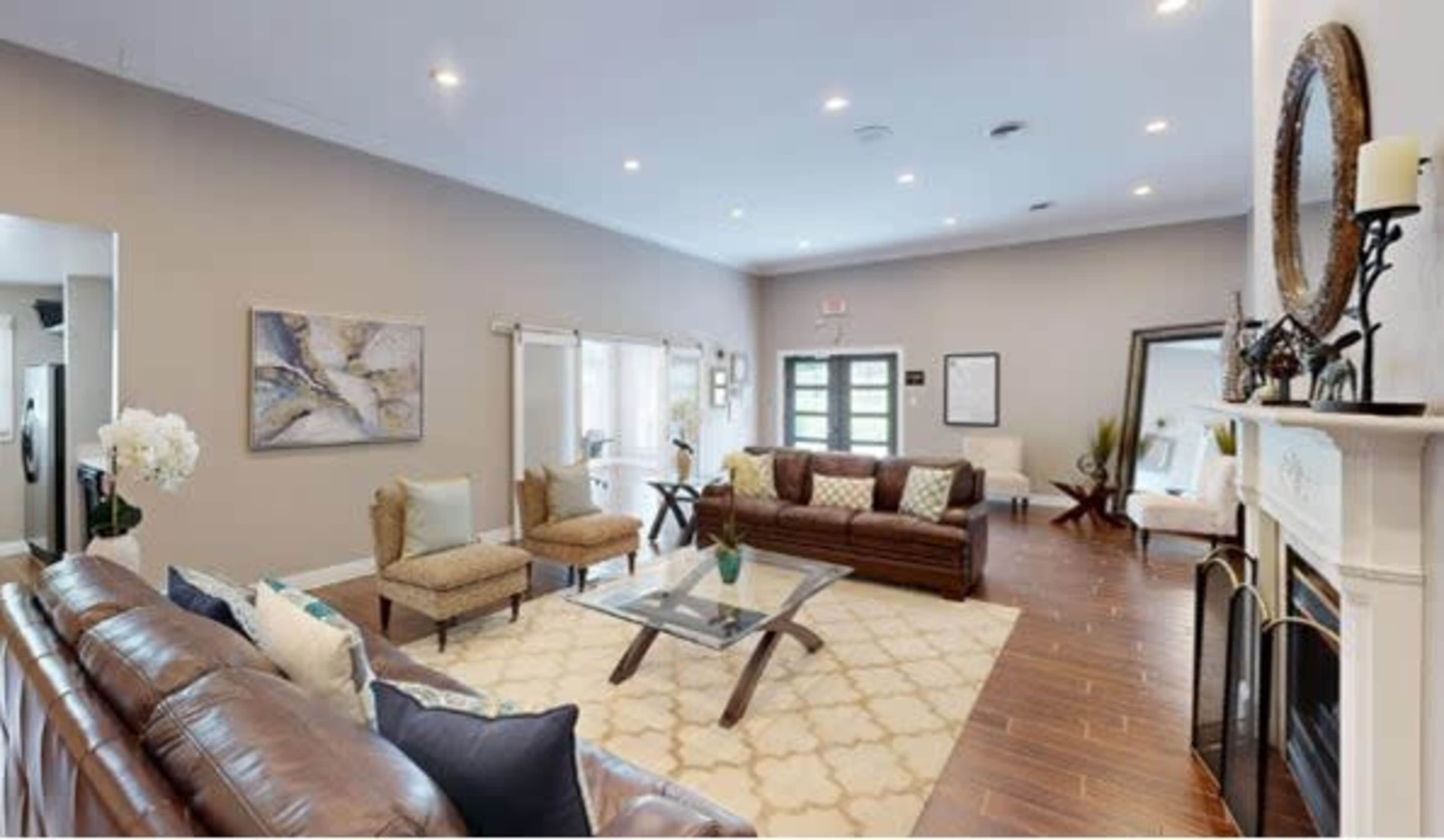 A spacious living room featuring two leather sofas, a glass coffee table, and decorative artwork on the walls, with large windows allowing natural light in.