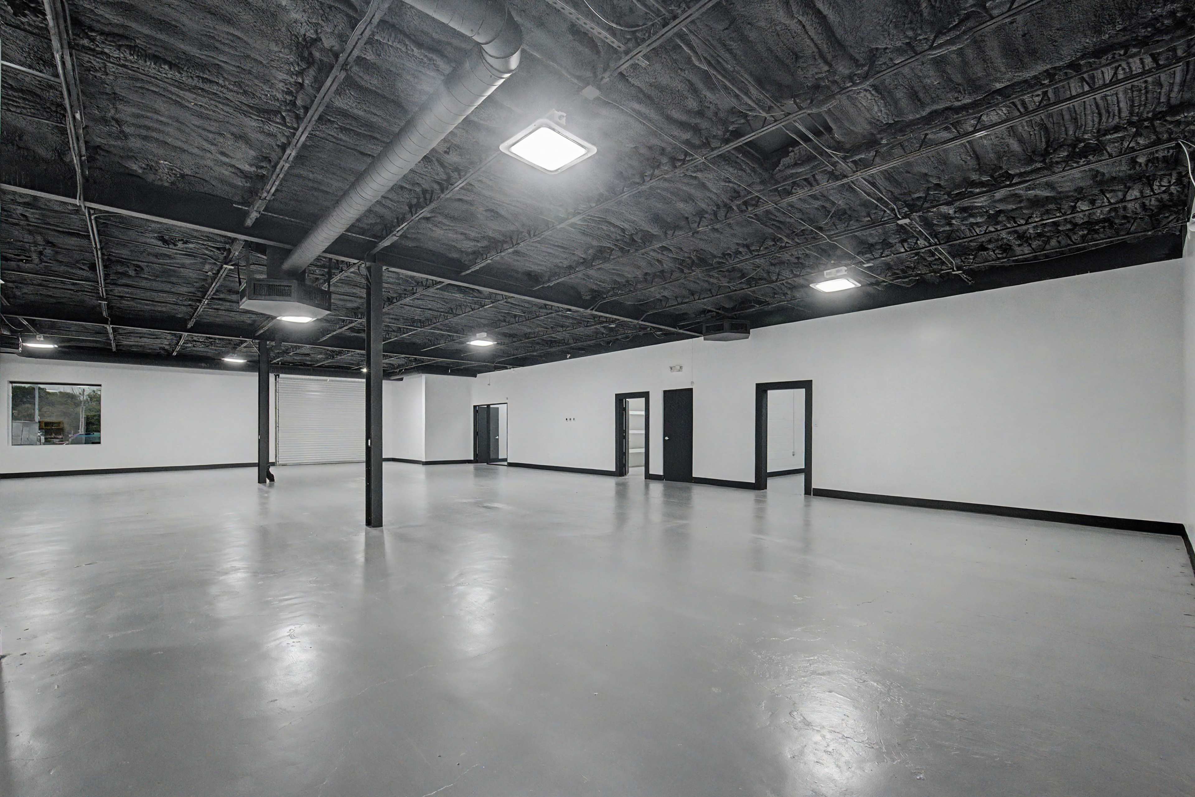 The image shows an empty, industrial-style interior space with a gray concrete floor, exposed ceiling, and several doors leading to different areas.