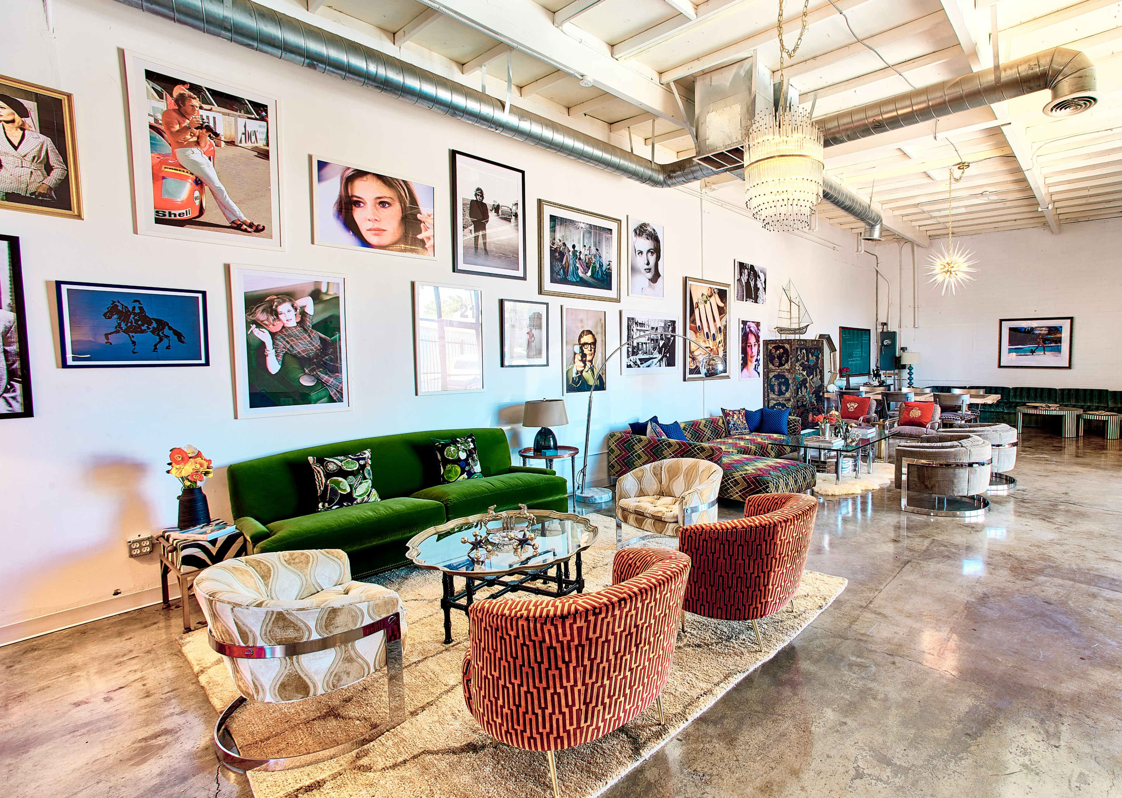 The image shows a spacious room with various seating options, including colorful chairs and couches, adorned with large framed photos on the walls.