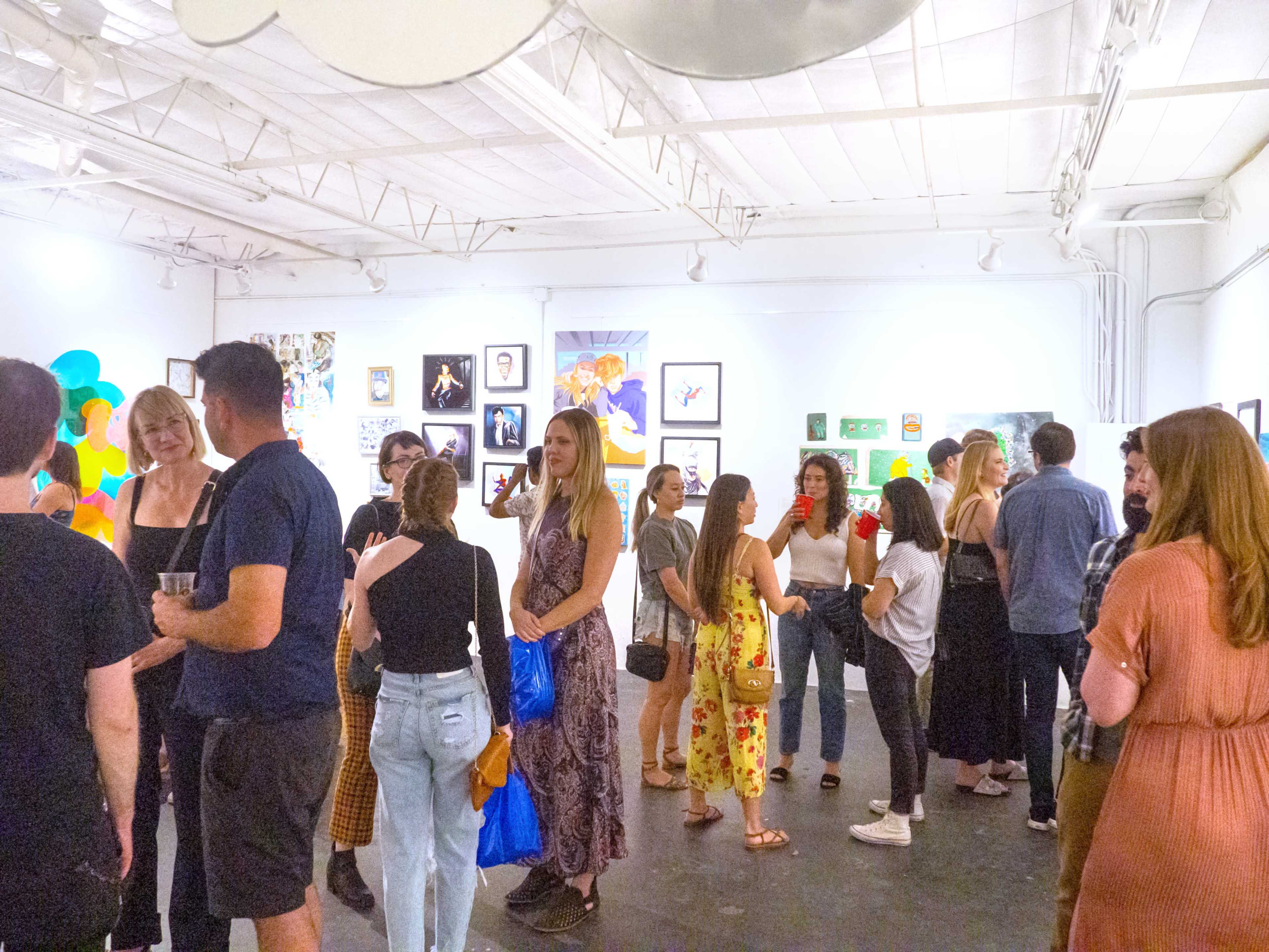 A group of people mingles in an art gallery filled with various artworks on the walls.