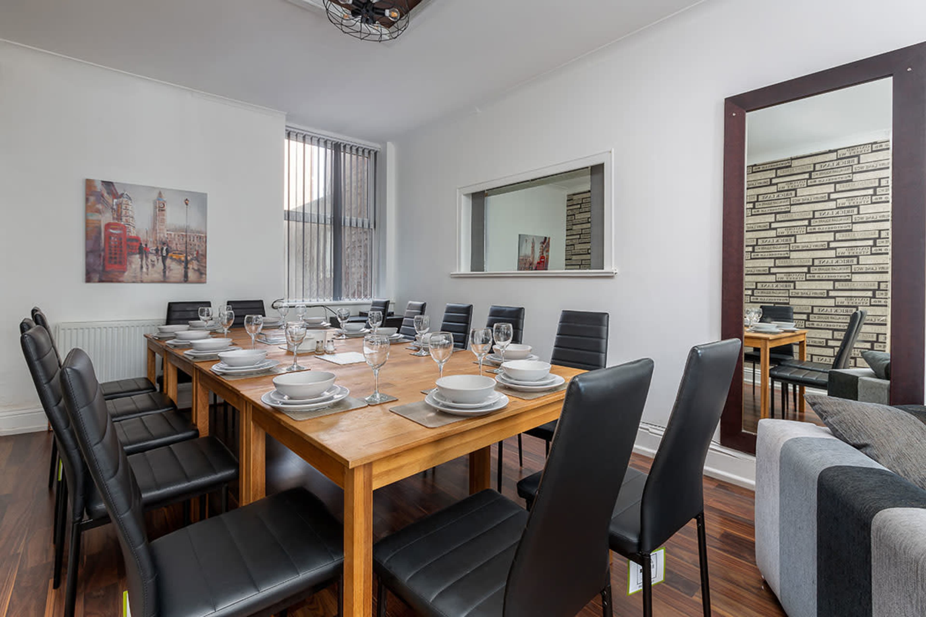 A spacious dining room features two long tables set with plates and glasses, surrounded by black chairs against a backdrop of white walls and decorative mirrors.