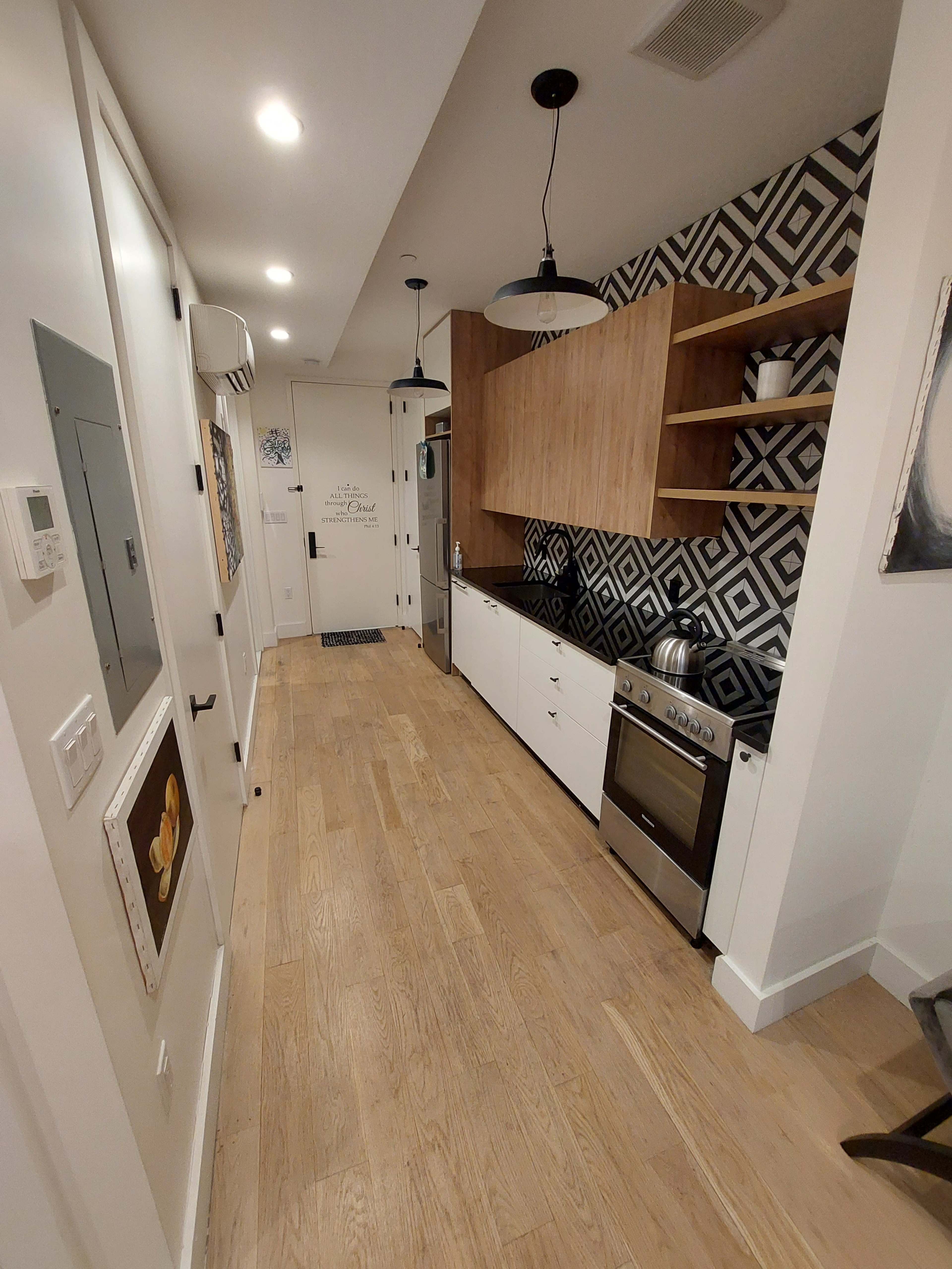 A modern kitchen with a sleek design, featuring a patterned backsplash, wooden shelves, and stainless steel appliances.