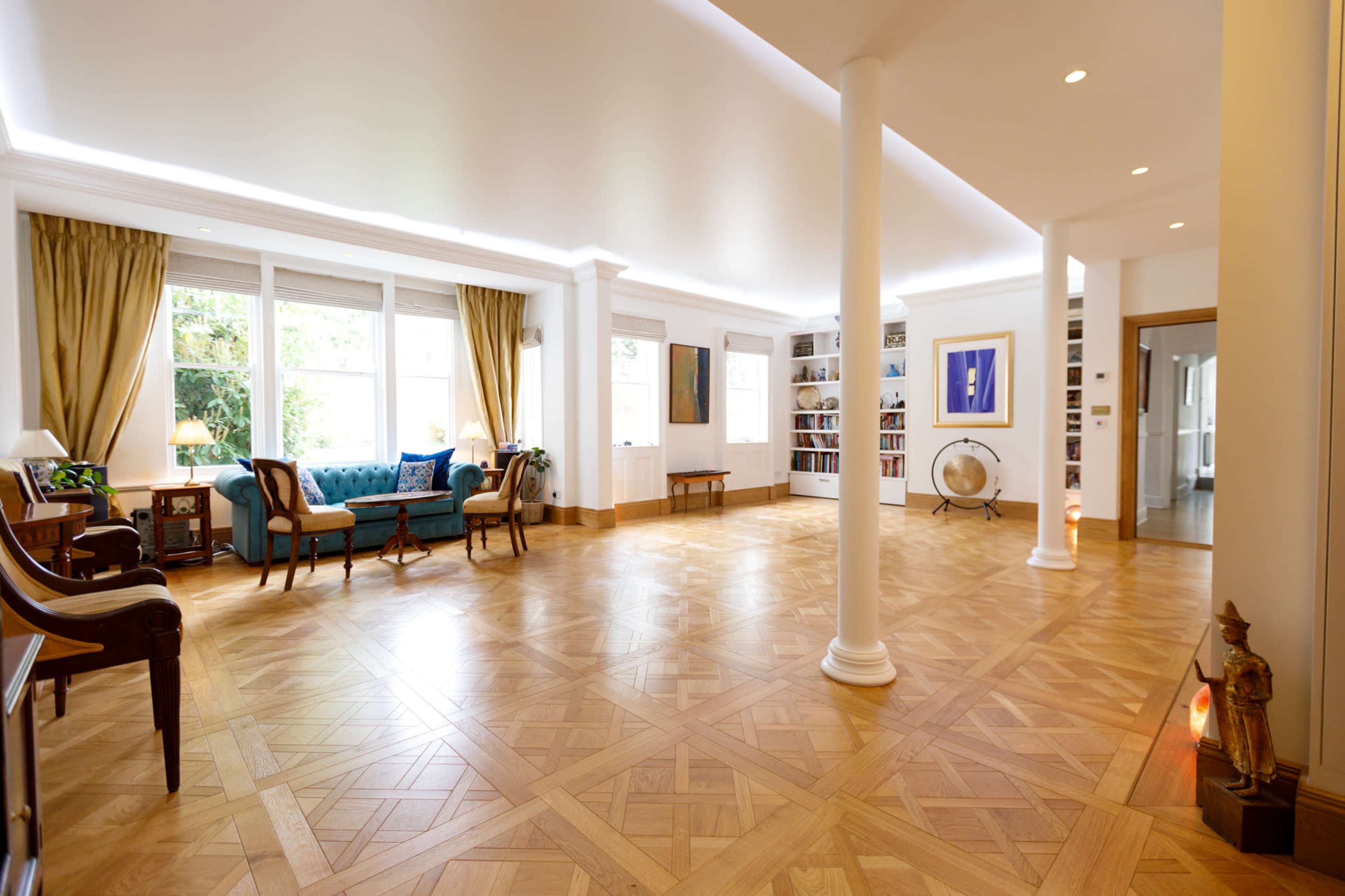 A spacious living room with wooden flooring, large windows, and a mix of modern and traditional furniture.