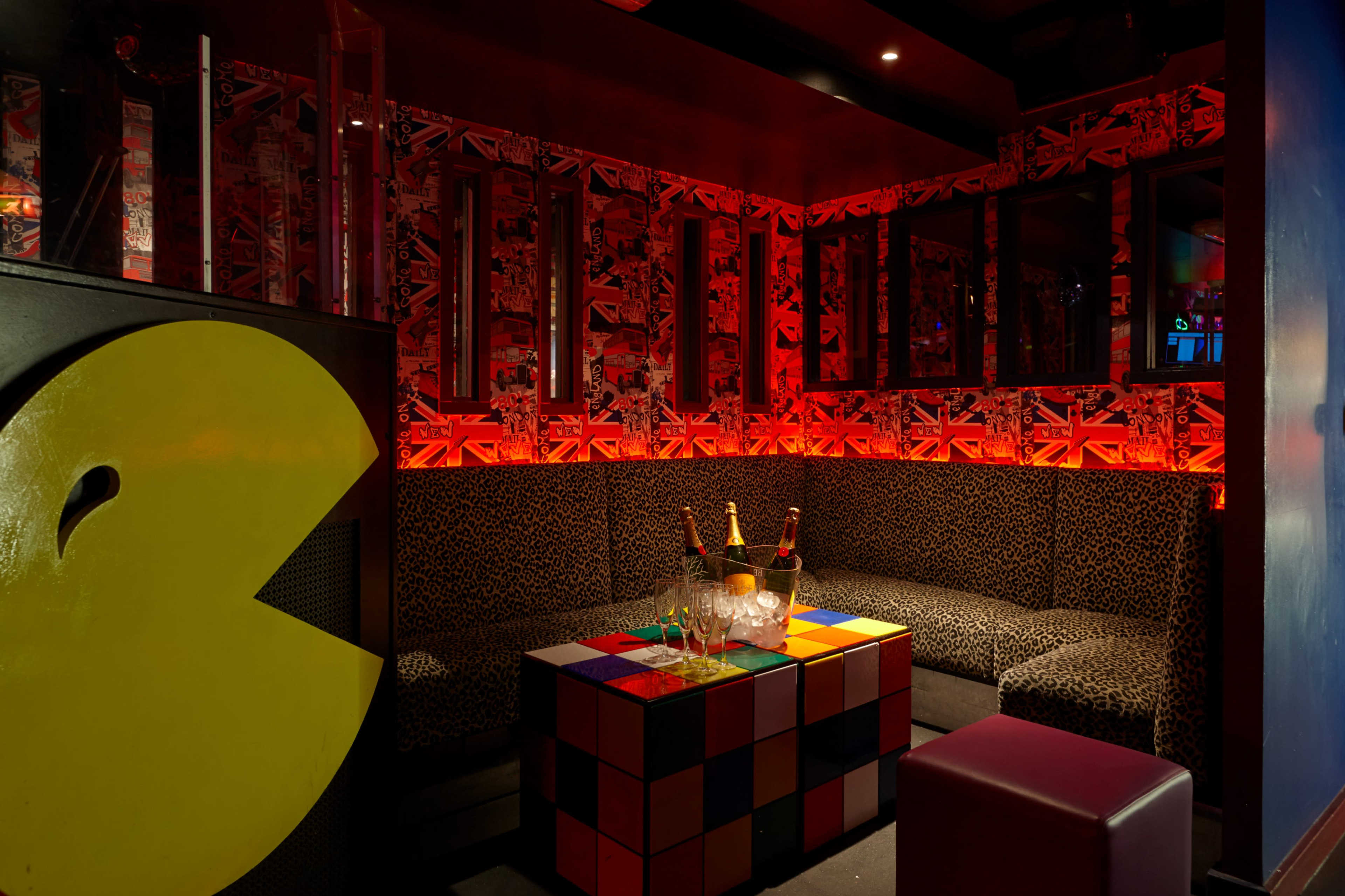 A vibrant lounge area with a curved seating arrangement, a colorful cube table, and bottles of champagne on display against a backdrop of wallpaper featuring the Union Jack.